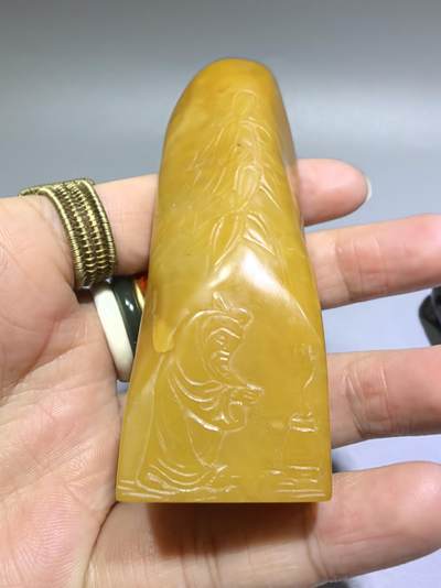 田黄石线雕印章
一两田黄十两金，市面上有“石帝”印石之王的美称。打灯肌理表皮组织可见密如之网的细萝卜纹，条理清晰。表皮可见一处天然裂格。博弈工，收藏级。尺寸:7.2cm*2.7cm克重:100.4g