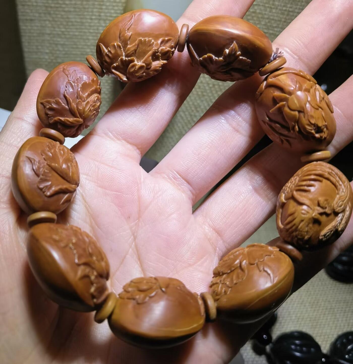 纯手工橄榄核浮雕凤穿牡丹男款手串佛珠，三花扁核浮雕凤穿牡丹花瓣雕刻栩栩如生，花瓣花蕊清晰渐层，扁核需要在不同面连贯雕刻，考验雕刻师的雕刻技术可见清晰留刀痕尺寸：18宽mm*24长mm