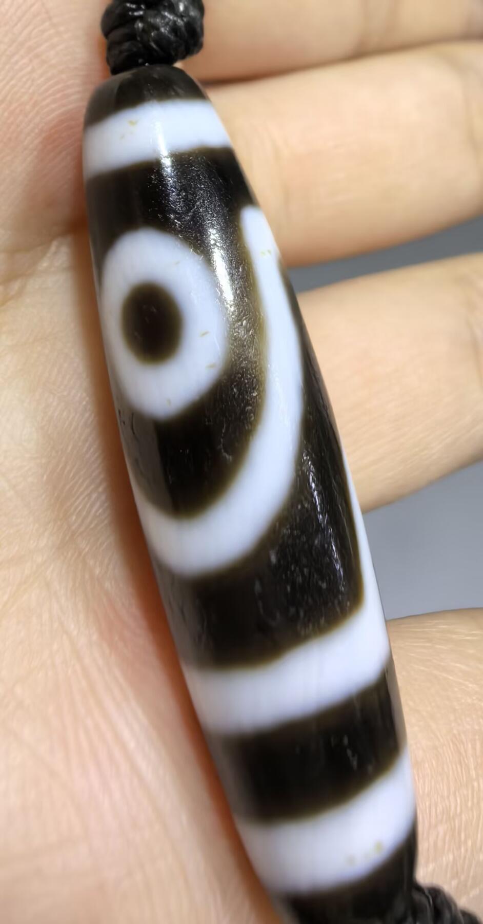 行运二眼天珠手链纯手工珠男女款手串
此款二眼天珠，是行运家早期品相，属于黑白品相，但是行运家天珠的特点就黑线部分远看是黑，上了倍镜以后是深褐色，珠体表面可见细风化纹，手工绘制图腾。
​尺寸:3.8*1.0cm
​