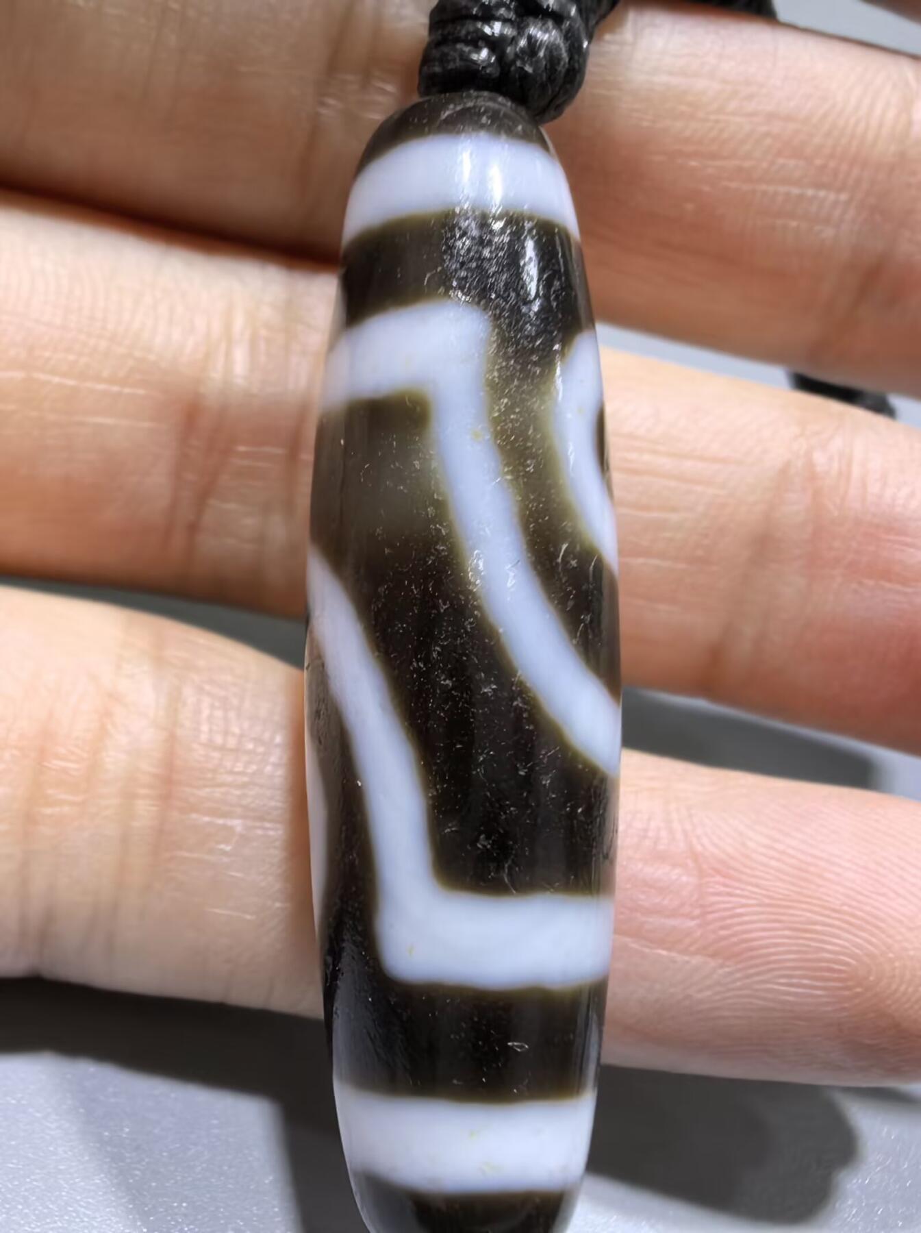行运二眼天珠手链纯手工珠男女款手串
此款二眼天珠，是行运家早期品相，属于黑白品相，但是行运家天珠的特点就黑线部分远看是黑，上了倍镜以后是深褐色，珠体表面可见细风化纹，手工绘制图腾。
​尺寸:3.8*1.0cm
​
