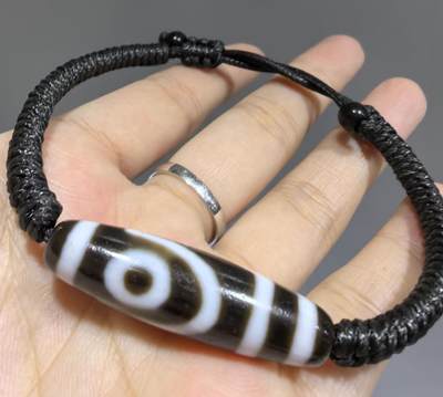 行运二眼天珠手链纯手工珠男女款手串
此款二眼天珠，是行运家早期品相，属于黑白品相，但是行运家天珠的特点就黑线部分远看是黑，上了倍镜以后是深褐色，珠体表面可见细风化纹，手工绘制图腾。
​尺寸:3.8*1.0cm
​