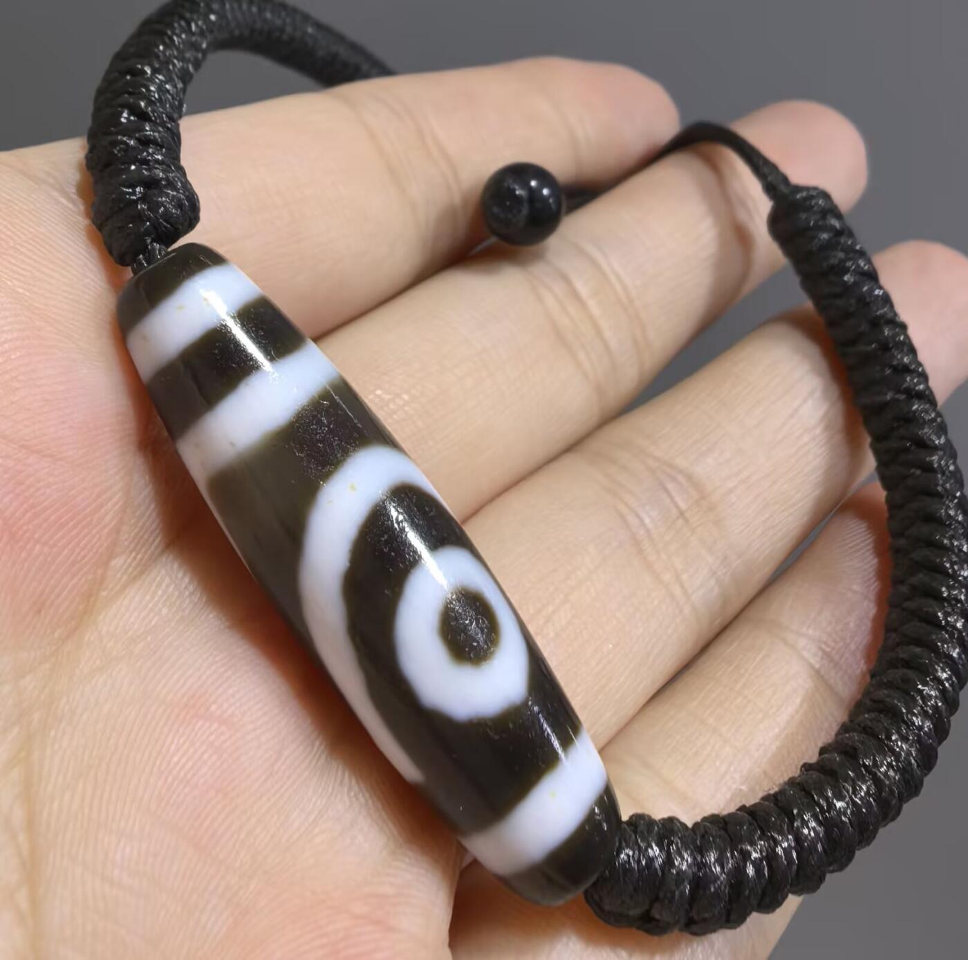 行运二眼天珠手链纯手工珠男女款手串
此款二眼天珠，是行运家早期品相，属于黑白品相，但是行运家天珠的特点就黑线部分远看是黑，上了倍镜以后是深褐色，珠体表面可见细风化纹，手工绘制图腾。
​尺寸:3.8*1.0cm
​