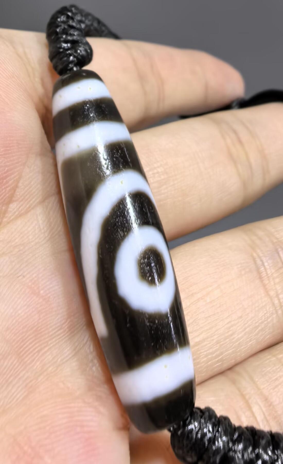 行运二眼天珠手链纯手工珠男女款手串
此款二眼天珠，是行运家早期品相，属于黑白品相，但是行运家天珠的特点就黑线部分远看是黑，上了倍镜以后是深褐色，珠体表面可见细风化纹，手工绘制图腾。
​尺寸:3.8*1.0cm
​