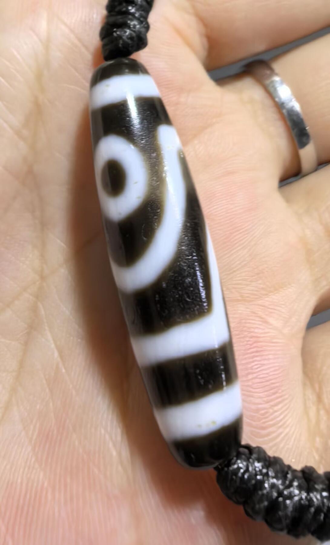 行运二眼天珠手链纯手工珠男女款手串
此款二眼天珠，是行运家早期品相，属于黑白品相，但是行运家天珠的特点就黑线部分远看是黑，上了倍镜以后是深褐色，珠体表面可见细风化纹，手工绘制图腾。
​尺寸:3.8*1.0cm
​