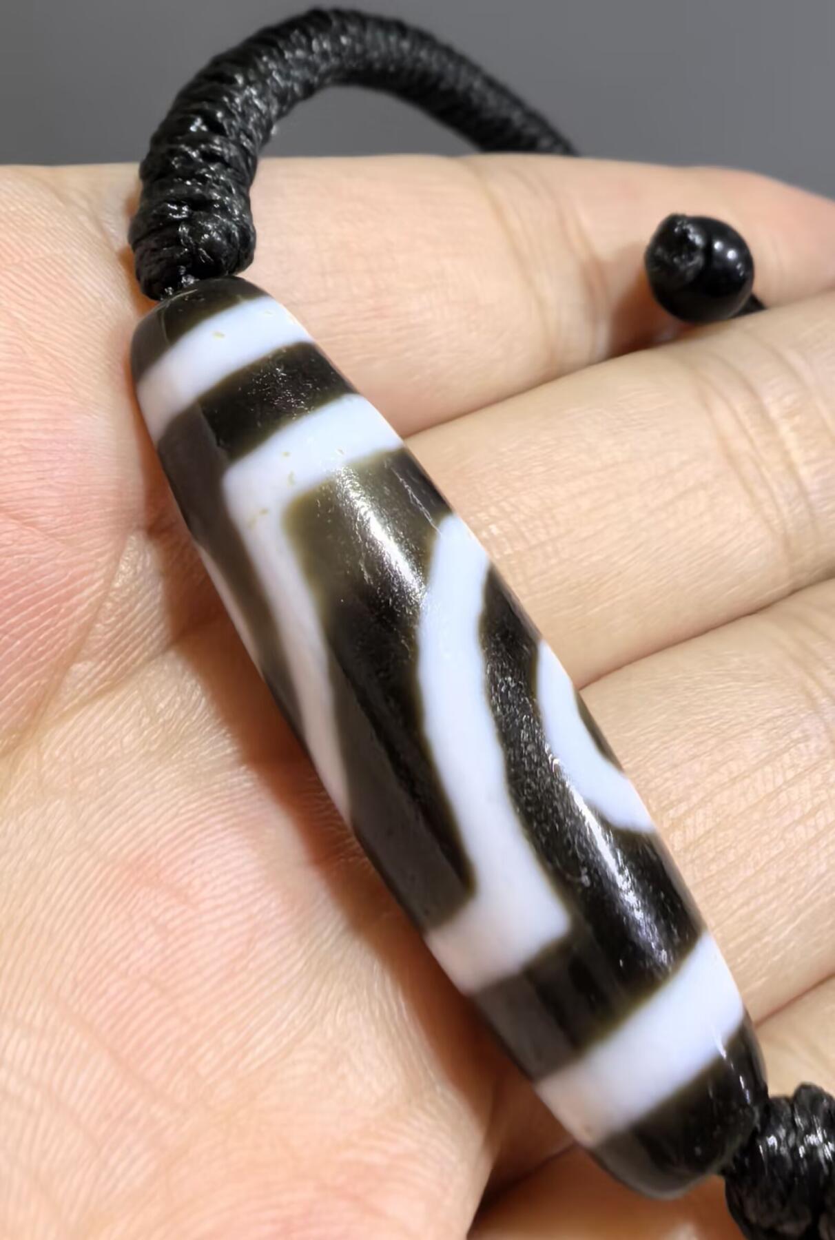 行运二眼天珠手链纯手工珠男女款手串
此款二眼天珠，是行运家早期品相，属于黑白品相，但是行运家天珠的特点就黑线部分远看是黑，上了倍镜以后是深褐色，珠体表面可见细风化纹，手工绘制图腾。
​尺寸:3.8*1.0cm
​