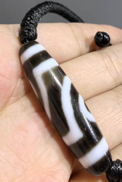 行运二眼天珠手链纯手工珠男女款手串
此款二眼天珠，是行运家早期品相，属于黑白品相，但是行运家天珠的特点就黑线部分远看是黑，上了倍镜以后是深褐色，珠体表面可见细风化纹，手工绘制图腾。
​尺寸:3.8*1.0cm
​