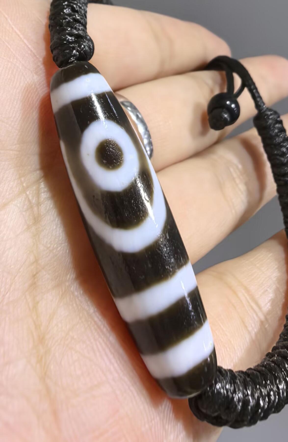 行运二眼天珠手链纯手工珠男女款手串
此款二眼天珠，是行运家早期品相，属于黑白品相，但是行运家天珠的特点就黑线部分远看是黑，上了倍镜以后是深褐色，珠体表面可见细风化纹，手工绘制图腾。
​尺寸:3.8*1.0cm
​