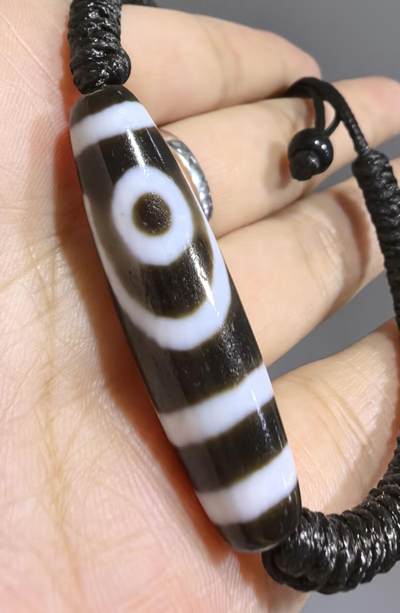 行运二眼天珠手链纯手工珠男女款手串
此款二眼天珠，是行运家早期品相，属于黑白品相，但是行运家天珠的特点就黑线部分远看是黑，上了倍镜以后是深褐色，珠体表面可见细风化纹，手工绘制图腾。
​尺寸:3.8*1.0cm
​