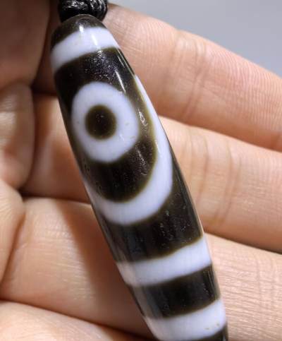 行运二眼天珠手链纯手工珠男女款手串
此款二眼天珠，是行运家早期品相，属于黑白品相，但是行运家天珠的特点就黑线部分远看是黑，上了倍镜以后是深褐色，珠体表面可见细风化纹，手工绘制图腾。
​尺寸:3.8*1.0cm
​