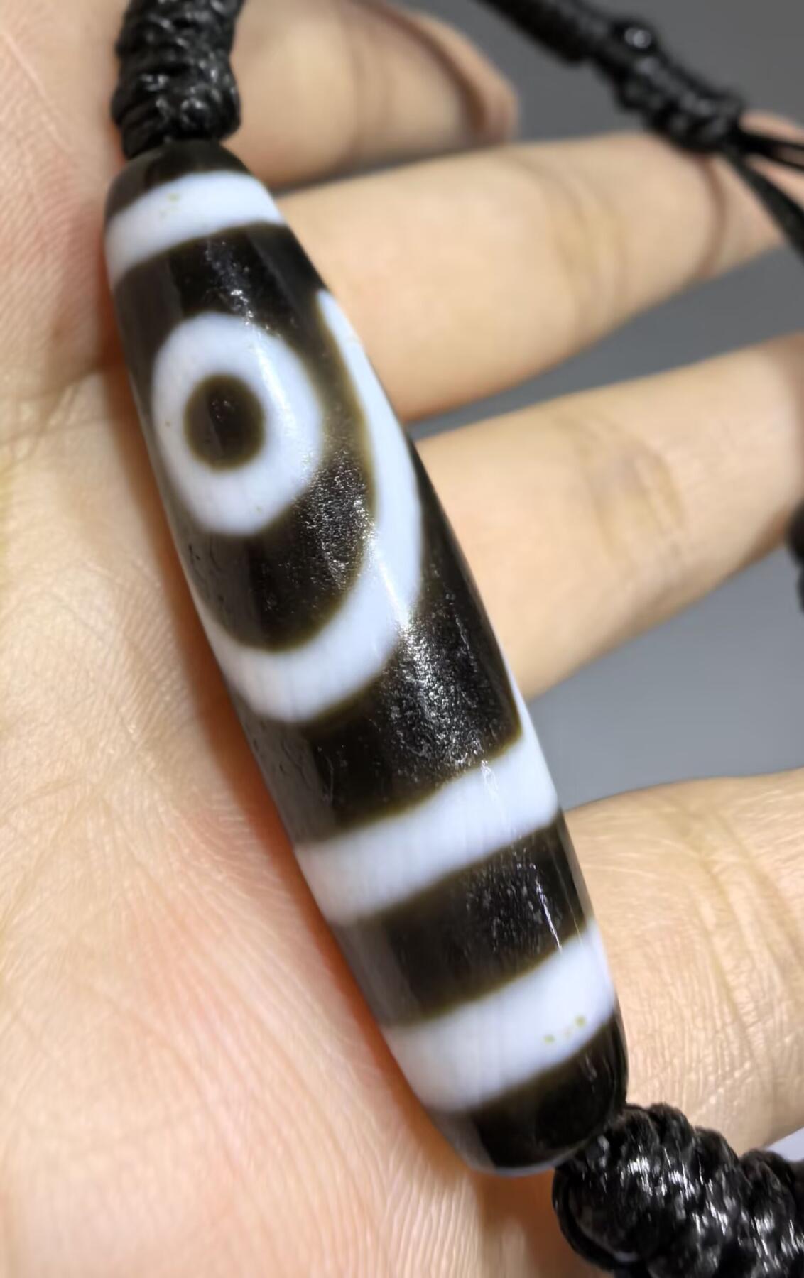 行运二眼天珠手链纯手工珠男女款手串
此款二眼天珠，是行运家早期品相，属于黑白品相，但是行运家天珠的特点就黑线部分远看是黑，上了倍镜以后是深褐色，珠体表面可见细风化纹，手工绘制图腾。
​尺寸:3.8*1.0cm
​