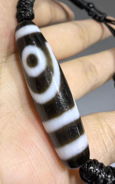 行运二眼天珠手链纯手工珠男女款手串
此款二眼天珠，是行运家早期品相，属于黑白品相，但是行运家天珠的特点就黑线部分远看是黑，上了倍镜以后是深褐色，珠体表面可见细风化纹，手工绘制图腾。
​尺寸:3.8*1.0cm
​