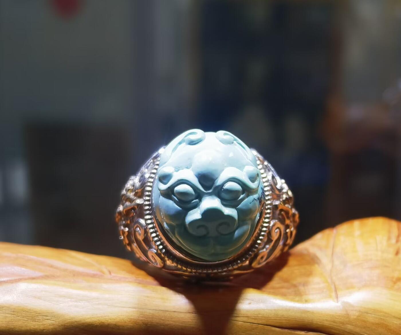 纯天然原矿松石雕刻兽面戒指男款，纯天然原矿松石能做雕刻要求瓷度密度比较高。松石瓷度不够，在雕刻的过程中容易松散，裸石干净漂亮。纯手工雕刻。霸气侧漏。尺寸:16mm×14mm*8mm纯银镂空镶嵌可调节指圈。
