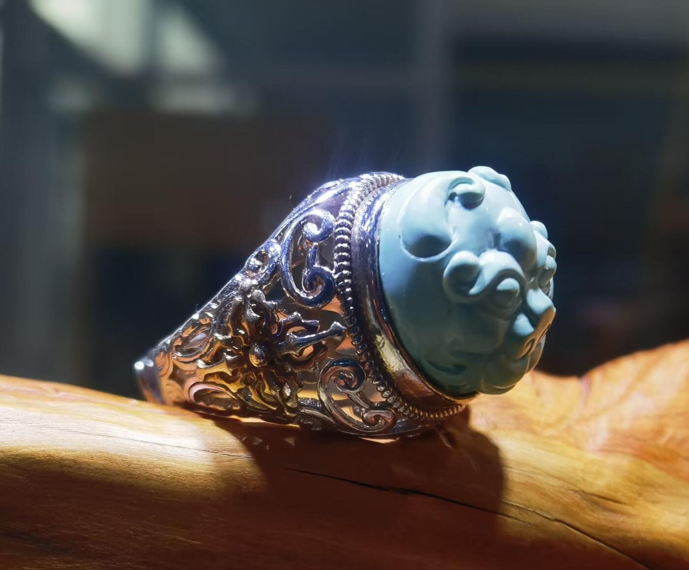 纯天然原矿松石雕刻兽面戒指男款，纯天然原矿松石能做雕刻要求瓷度密度比较高。松石瓷度不够，在雕刻的过程中容易松散，裸石干净漂亮。纯手工雕刻。霸气侧漏。尺寸:16mm×14mm*8mm纯银镂空镶嵌可调节指圈。