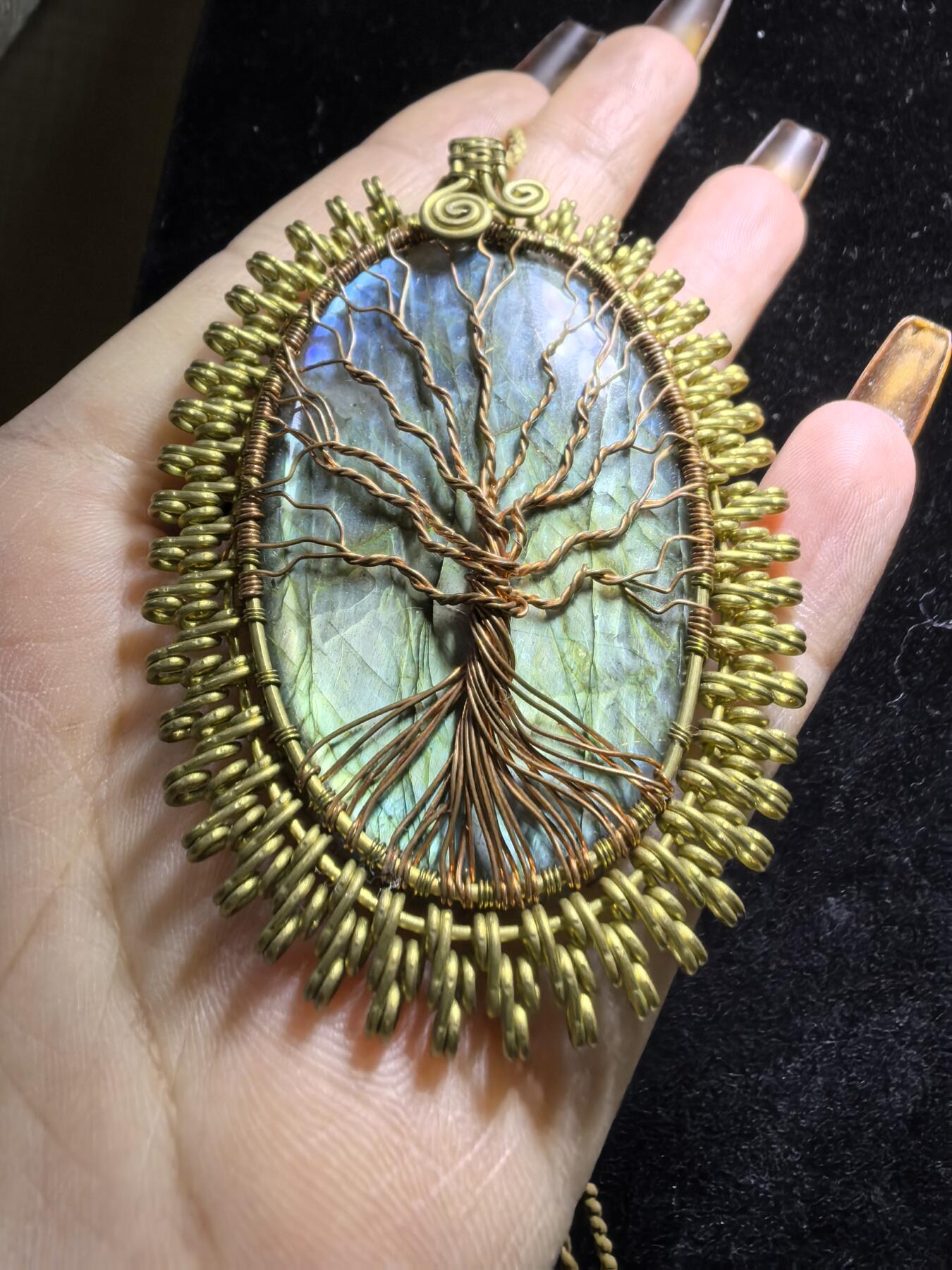 委内瑞拉国际友人纯手工绕丝工艺《灵光生命之树吊坠》男女款
以铜线手工编织的生命之树坐落在蓝火拉布拉多长石之上，整件作品带来更强的净化与守护能量。采用巴西编绳，可自由调节长度。
一件汇聚光、根与灵性的护符。
​尺寸：7.1cm*5.1cm*0.8cm每一款都是独一无二，非量产。
​天然有机宝石内部无法避免结构纹理等，介意勿扰！