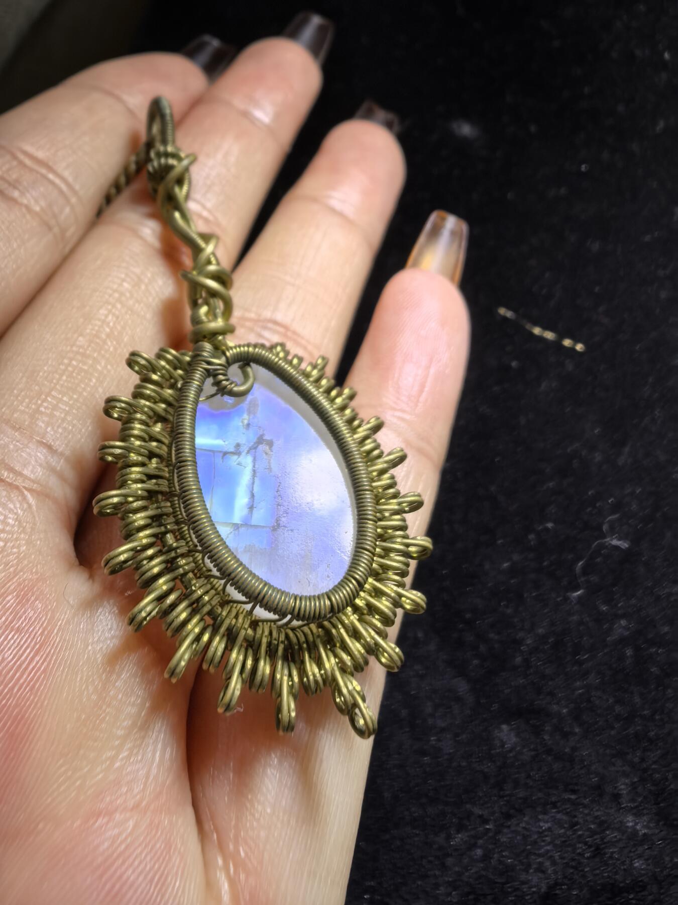 来自委内瑞拉国际友人手工绕丝工艺，月光石吊坠 从不同角度观察，它展现出不同的色彩魅力。有时是极光般的梦幻色彩，有时是少女般的温柔色彩，还有时是落日晚霞般的绚烂色彩。 佩戴与众不同独一无二。 尺寸:2.9cm*2.6cm*1.9cm ​