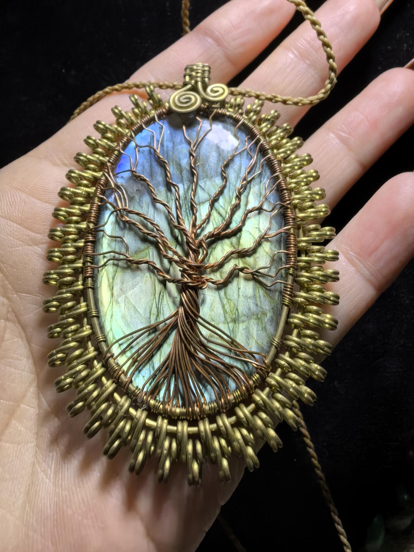 委内瑞拉国际友人纯手工绕丝工艺《灵光生命之树吊坠》男女款
以铜线手工编织的生命之树坐落在蓝火拉布拉多长石之上，整件作品带来更强的净化与守护能量。采用巴西编绳，可自由调节长度。
一件汇聚光、根与灵性的护符。
​尺寸：7.1cm*5.1cm*0.8cm每一款都是独一无二，非量产。
​天然有机宝石内部无法避免结构纹理等，介意勿扰！