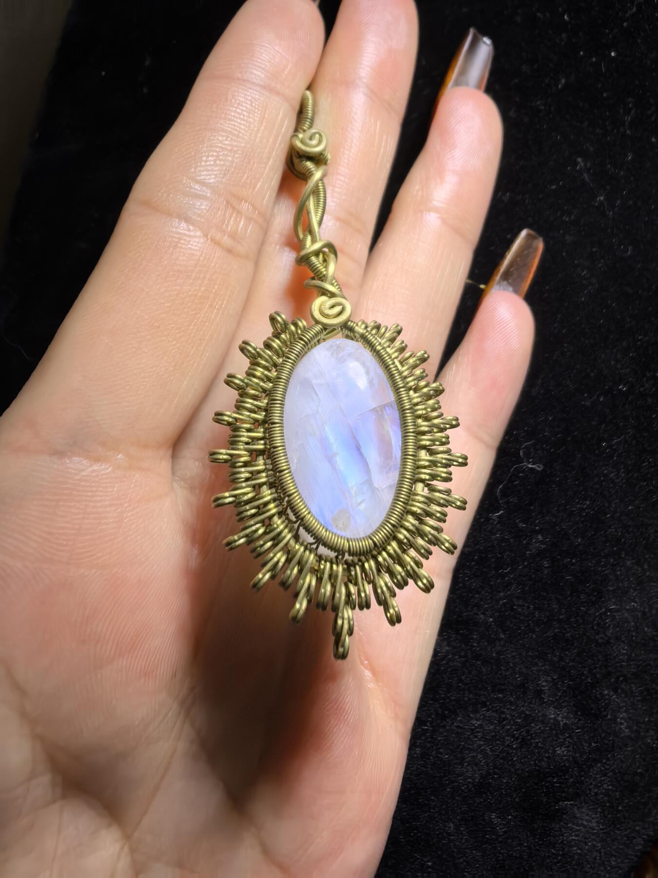 来自委内瑞拉国际友人手工绕丝工艺，月光石吊坠 从不同角度观察，它展现出不同的色彩魅力。有时是极光般的梦幻色彩，有时是少女般的温柔色彩，还有时是落日晚霞般的绚烂色彩。 佩戴与众不同独一无二。 尺寸:2.9cm*2.6cm*1.9cm ​