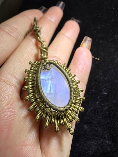 来自委内瑞拉国际友人手工绕丝工艺，月光石吊坠 从不同角度观察，它展现出不同的色彩魅力。有时是极光般的梦幻色彩，有时是少女般的温柔色彩，还有时是落日晚霞般的绚烂色彩。 佩戴与众不同独一无二。 尺寸:2.9cm*2.6cm*1.9cm ​