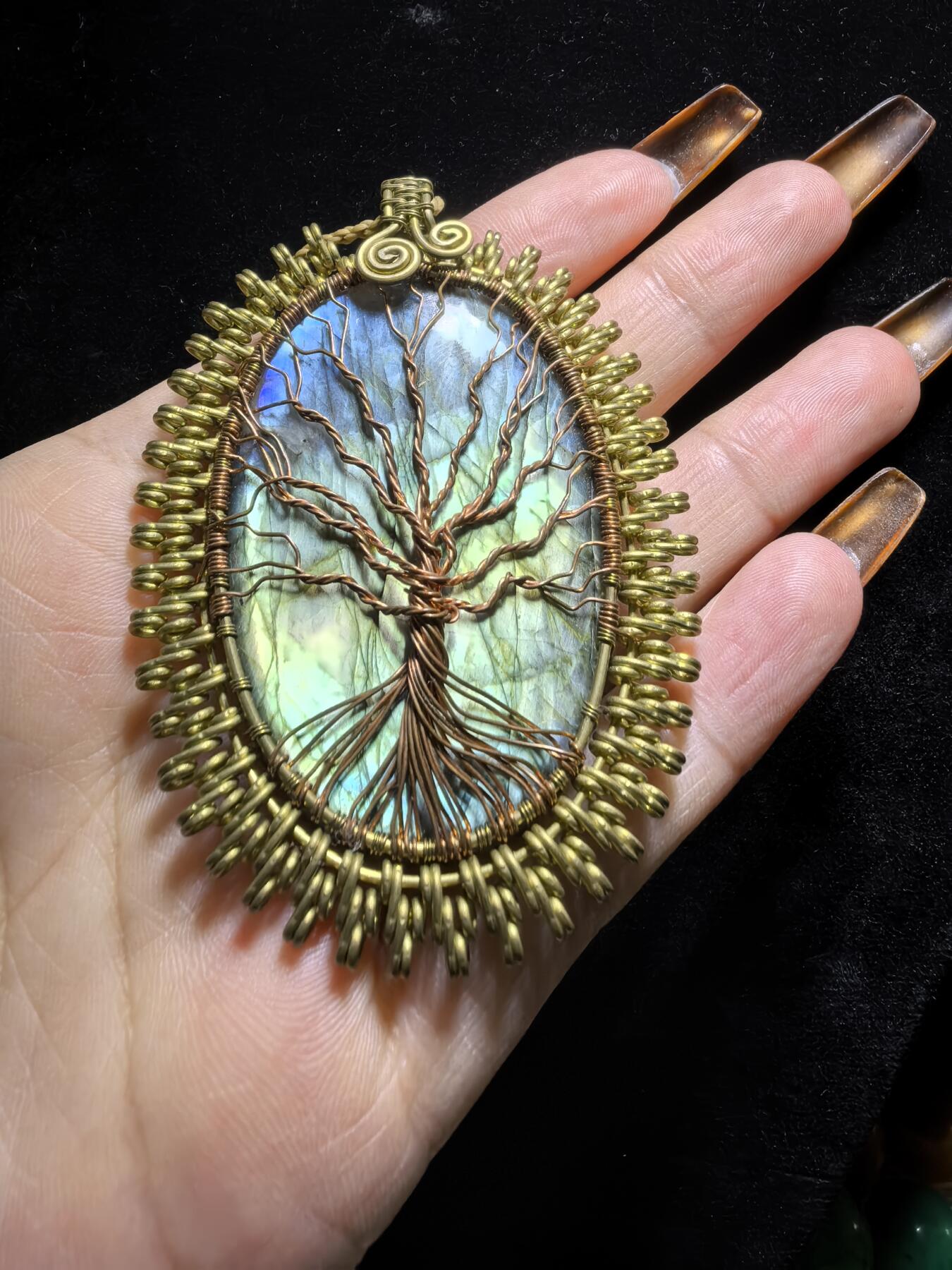 委内瑞拉国际友人纯手工绕丝工艺《灵光生命之树吊坠》男女款
以铜线手工编织的生命之树坐落在蓝火拉布拉多长石之上，整件作品带来更强的净化与守护能量。采用巴西编绳，可自由调节长度。
一件汇聚光、根与灵性的护符。
​尺寸：7.1cm*5.1cm*0.8cm每一款都是独一无二，非量产。
​天然有机宝石内部无法避免结构纹理等，介意勿扰！