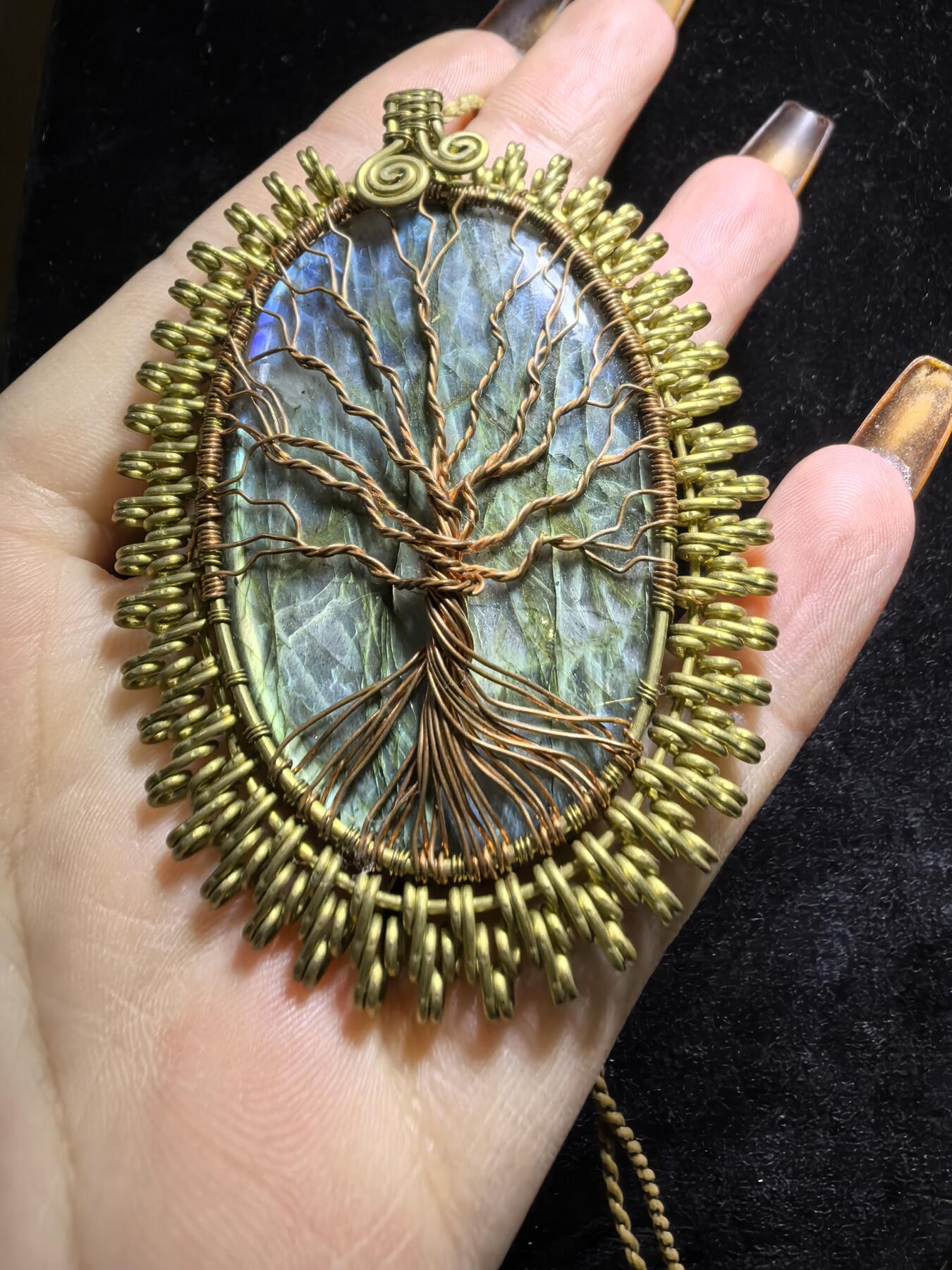 委内瑞拉国际友人纯手工绕丝工艺《灵光生命之树吊坠》男女款
以铜线手工编织的生命之树坐落在蓝火拉布拉多长石之上，整件作品带来更强的净化与守护能量。采用巴西编绳，可自由调节长度。
一件汇聚光、根与灵性的护符。
​尺寸：7.1cm*5.1cm*0.8cm每一款都是独一无二，非量产。
​天然有机宝石内部无法避免结构纹理等，介意勿扰！