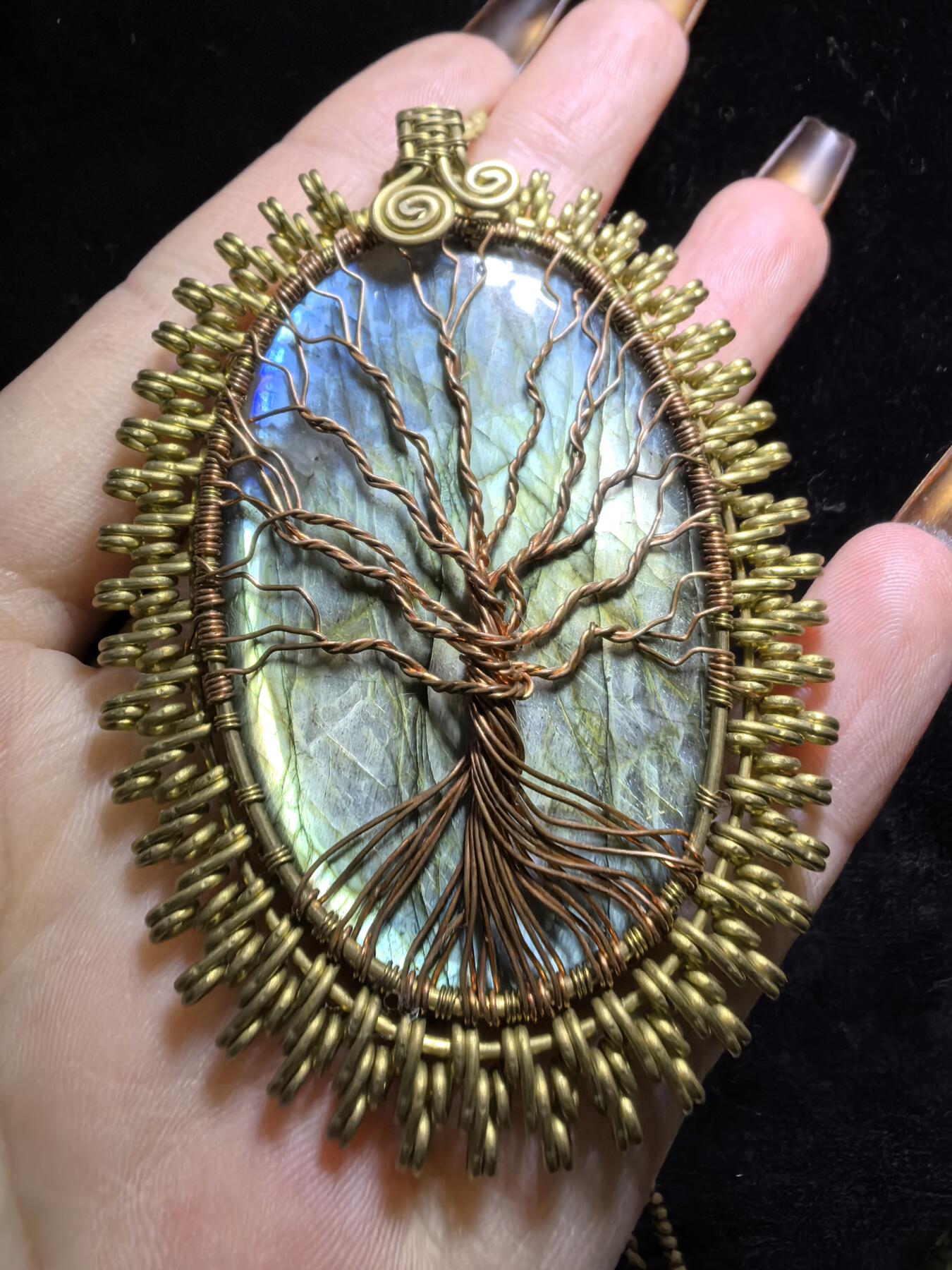 委内瑞拉国际友人纯手工绕丝工艺《灵光生命之树吊坠》男女款
以铜线手工编织的生命之树坐落在蓝火拉布拉多长石之上，整件作品带来更强的净化与守护能量。采用巴西编绳，可自由调节长度。
一件汇聚光、根与灵性的护符。
​尺寸：7.1cm*5.1cm*0.8cm每一款都是独一无二，非量产。
​天然有机宝石内部无法避免结构纹理等，介意勿扰！