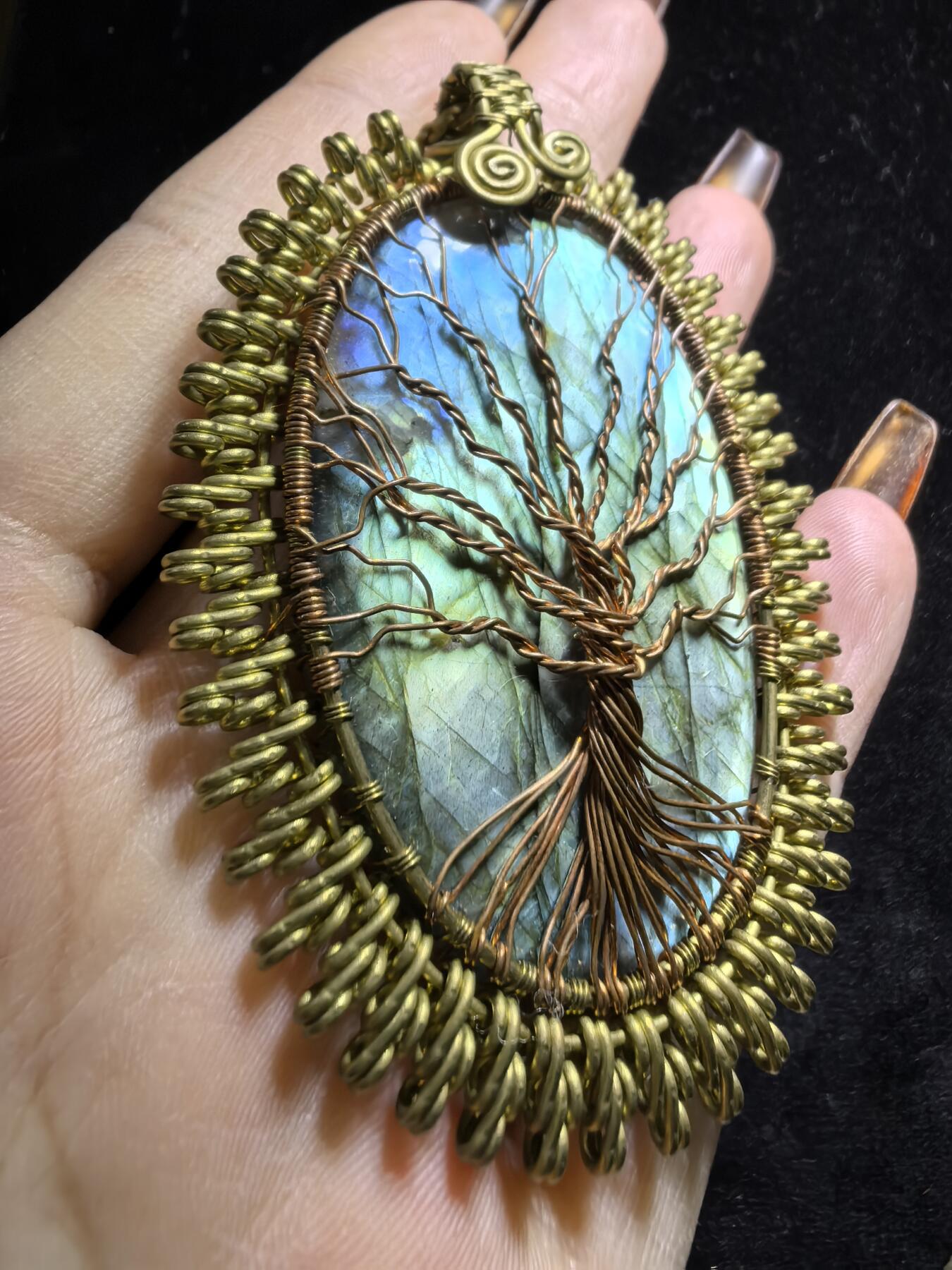 委内瑞拉国际友人纯手工绕丝工艺《灵光生命之树吊坠》男女款
以铜线手工编织的生命之树坐落在蓝火拉布拉多长石之上，整件作品带来更强的净化与守护能量。采用巴西编绳，可自由调节长度。
一件汇聚光、根与灵性的护符。
​尺寸：7.1cm*5.1cm*0.8cm每一款都是独一无二，非量产。
​天然有机宝石内部无法避免结构纹理等，介意勿扰！