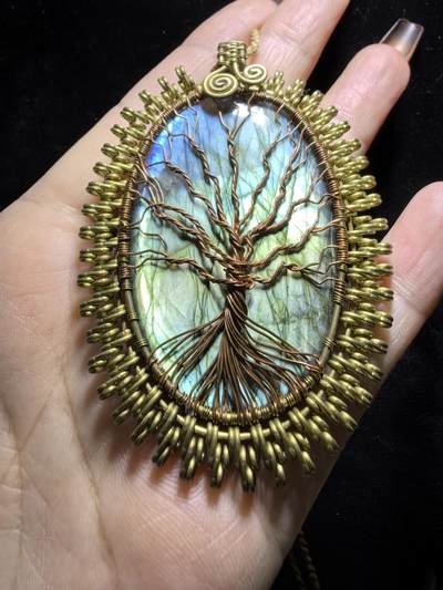 委内瑞拉国际友人纯手工绕丝工艺《灵光生命之树吊坠》男女款
以铜线手工编织的生命之树坐落在蓝火拉布拉多长石之上，整件作品带来更强的净化与守护能量。采用巴西编绳，可自由调节长度。
一件汇聚光、根与灵性的护符。
​尺寸：7.1cm*5.1cm*0.8cm每一款都是独一无二，非量产。
​天然有机宝石内部无法避免结构纹理等，介意勿扰！