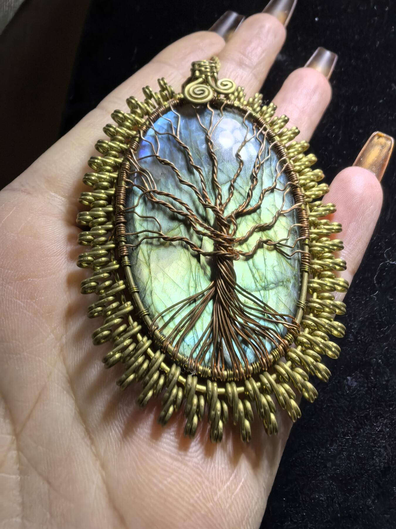 委内瑞拉国际友人纯手工绕丝工艺《灵光生命之树吊坠》男女款
以铜线手工编织的生命之树坐落在蓝火拉布拉多长石之上，整件作品带来更强的净化与守护能量。采用巴西编绳，可自由调节长度。
一件汇聚光、根与灵性的护符。
​尺寸：7.1cm*5.1cm*0.8cm每一款都是独一无二，非量产。
​天然有机宝石内部无法避免结构纹理等，介意勿扰！