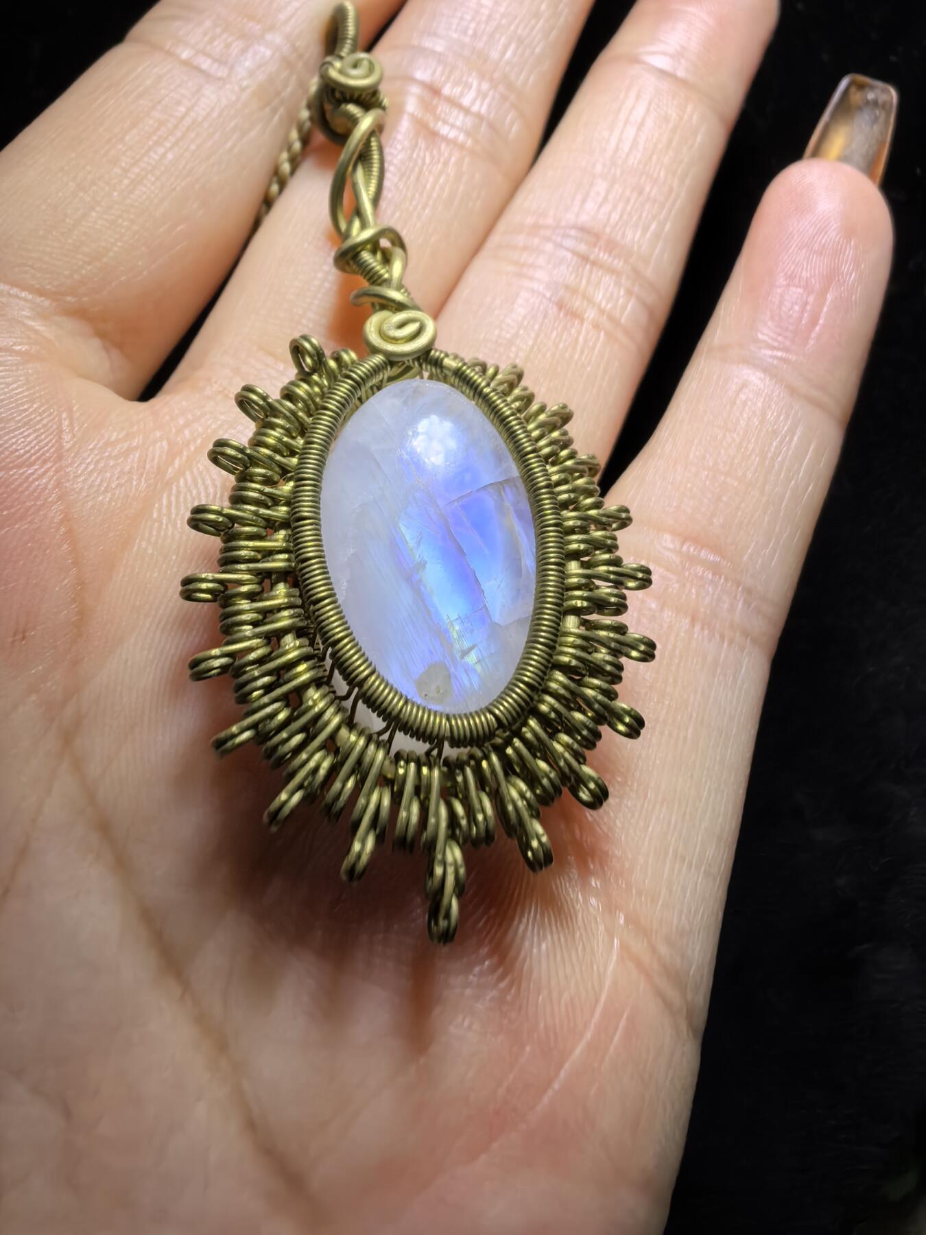 来自委内瑞拉国际友人手工绕丝工艺，月光石吊坠 从不同角度观察，它展现出不同的色彩魅力。有时是极光般的梦幻色彩，有时是少女般的温柔色彩，还有时是落日晚霞般的绚烂色彩。 佩戴与众不同独一无二。 尺寸:2.9cm*2.6cm*1.9cm ​