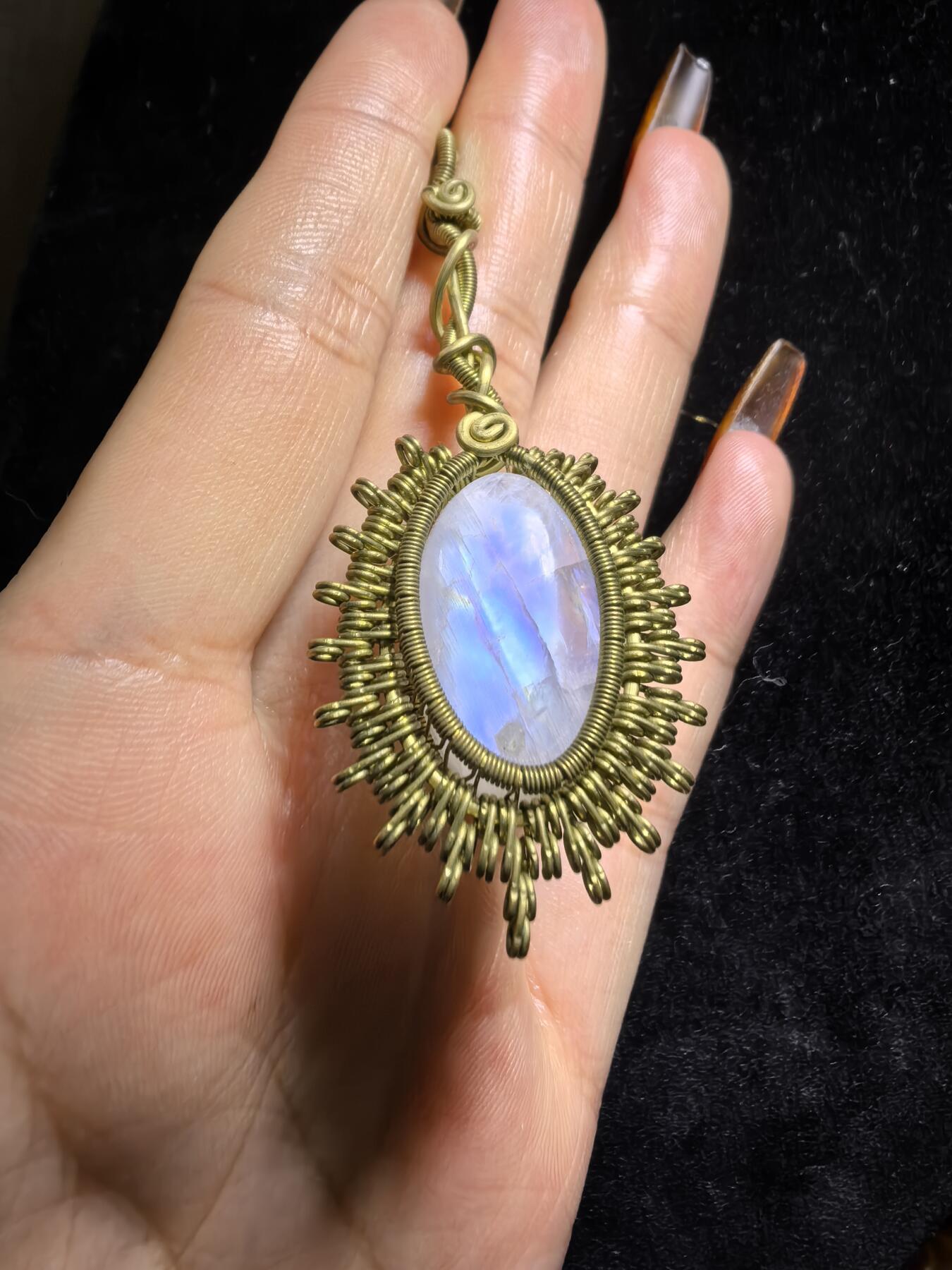 来自委内瑞拉国际友人手工绕丝工艺，月光石吊坠 从不同角度观察，它展现出不同的色彩魅力。有时是极光般的梦幻色彩，有时是少女般的温柔色彩，还有时是落日晚霞般的绚烂色彩。 佩戴与众不同独一无二。 尺寸:2.9cm*2.6cm*1.9cm ​