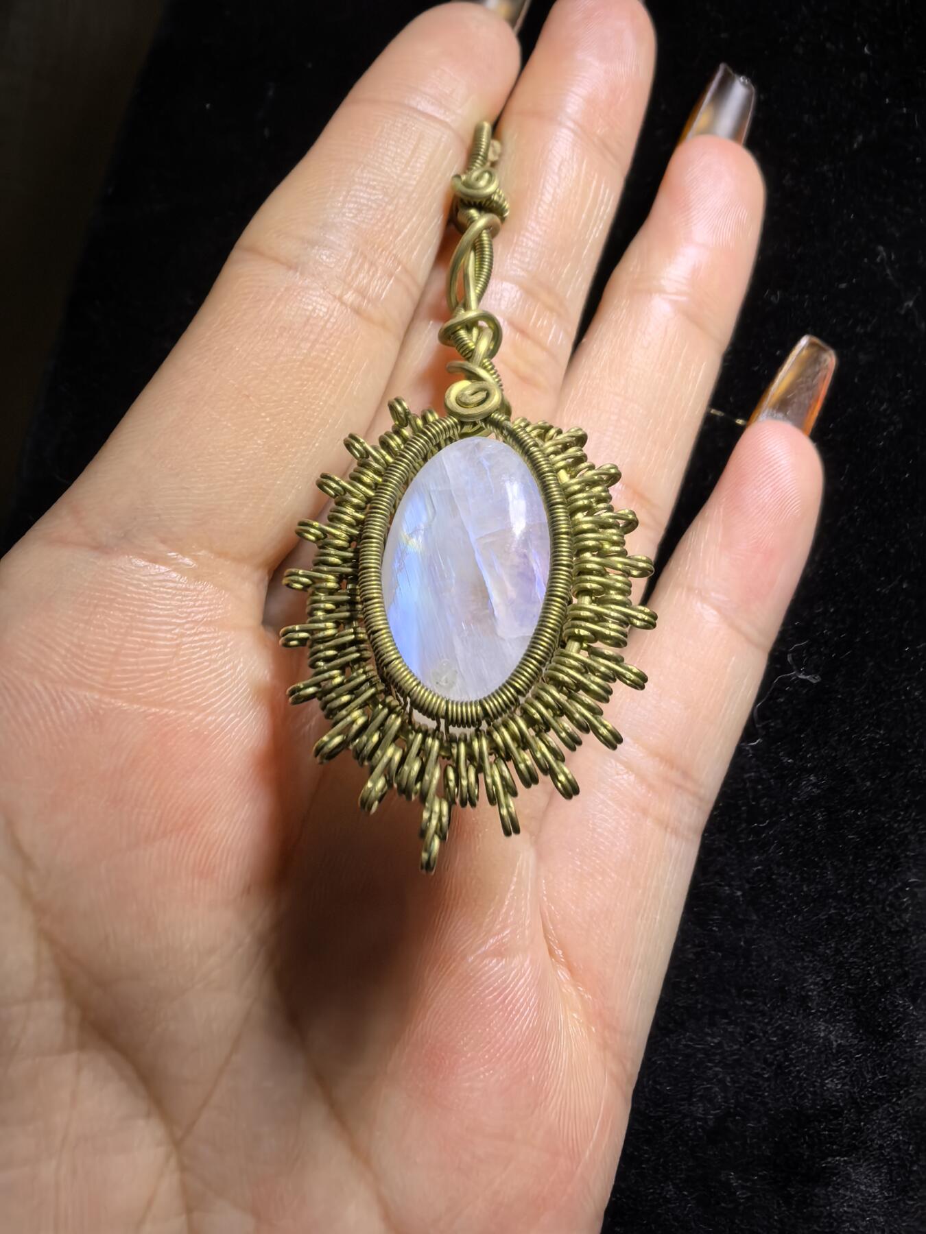 来自委内瑞拉国际友人手工绕丝工艺，月光石吊坠 从不同角度观察，它展现出不同的色彩魅力。有时是极光般的梦幻色彩，有时是少女般的温柔色彩，还有时是落日晚霞般的绚烂色彩。 佩戴与众不同独一无二。 尺寸:2.9cm*2.6cm*1.9cm ​