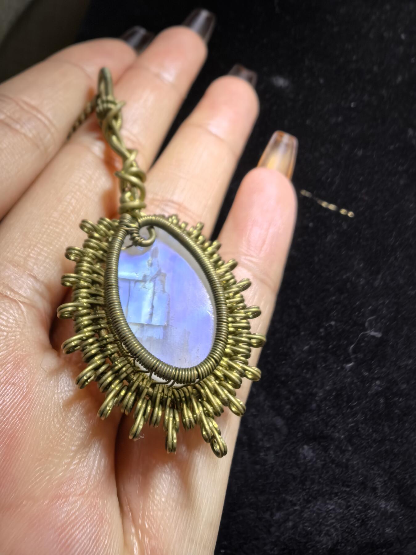 来自委内瑞拉国际友人手工绕丝工艺，月光石吊坠 从不同角度观察，它展现出不同的色彩魅力。有时是极光般的梦幻色彩，有时是少女般的温柔色彩，还有时是落日晚霞般的绚烂色彩。 佩戴与众不同独一无二。 尺寸:2.9cm*2.6cm*1.9cm ​