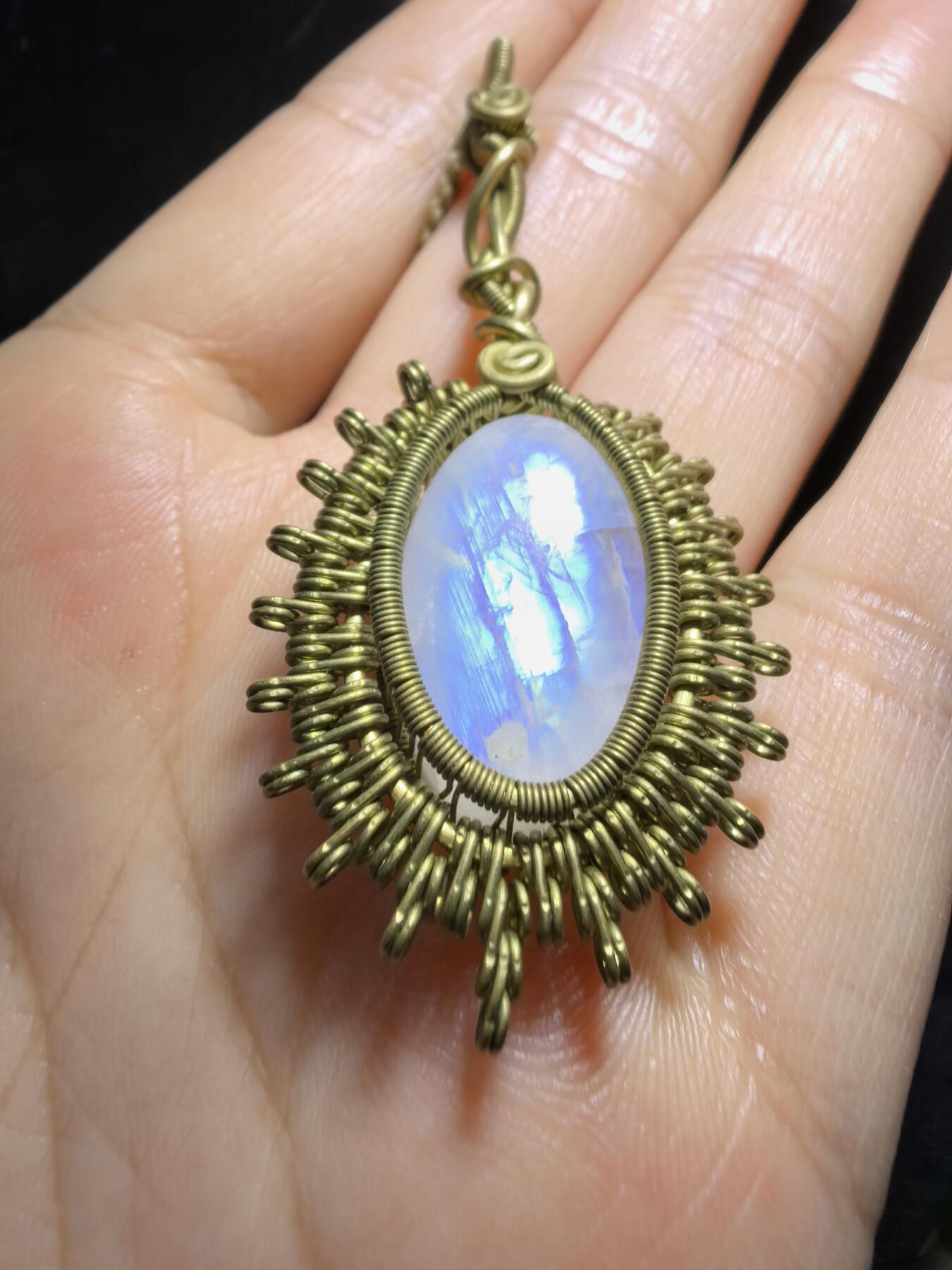 来自委内瑞拉国际友人手工绕丝工艺，月光石吊坠 从不同角度观察，它展现出不同的色彩魅力。有时是极光般的梦幻色彩，有时是少女般的温柔色彩，还有时是落日晚霞般的绚烂色彩。 佩戴与众不同独一无二。 尺寸:2.9cm*2.6cm*1.9cm ​