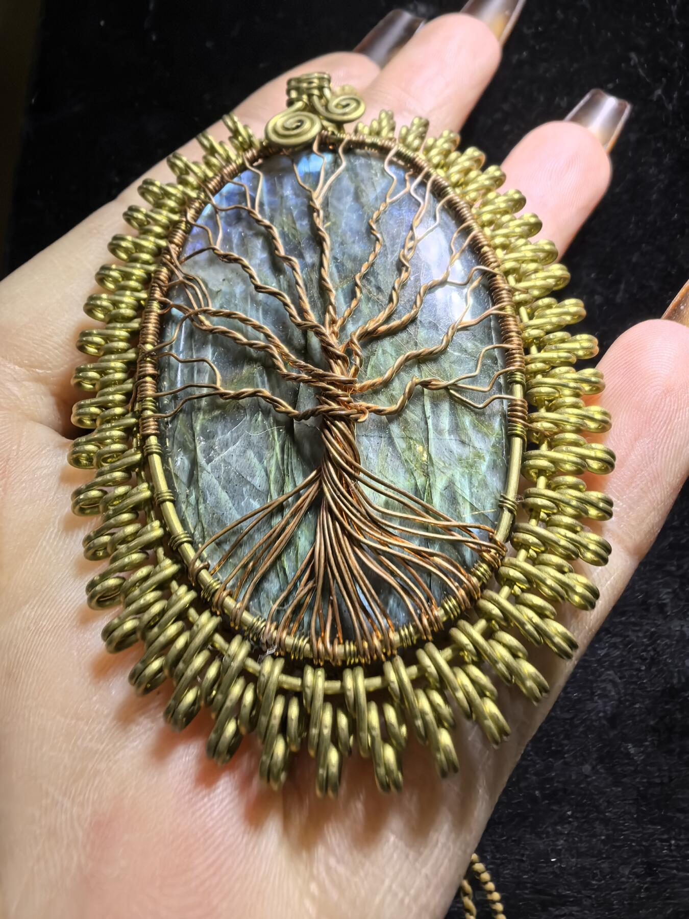 委内瑞拉国际友人纯手工绕丝工艺《灵光生命之树吊坠》男女款
以铜线手工编织的生命之树坐落在蓝火拉布拉多长石之上，整件作品带来更强的净化与守护能量。采用巴西编绳，可自由调节长度。
一件汇聚光、根与灵性的护符。
​尺寸：7.1cm*5.1cm*0.8cm每一款都是独一无二，非量产。
​天然有机宝石内部无法避免结构纹理等，介意勿扰！