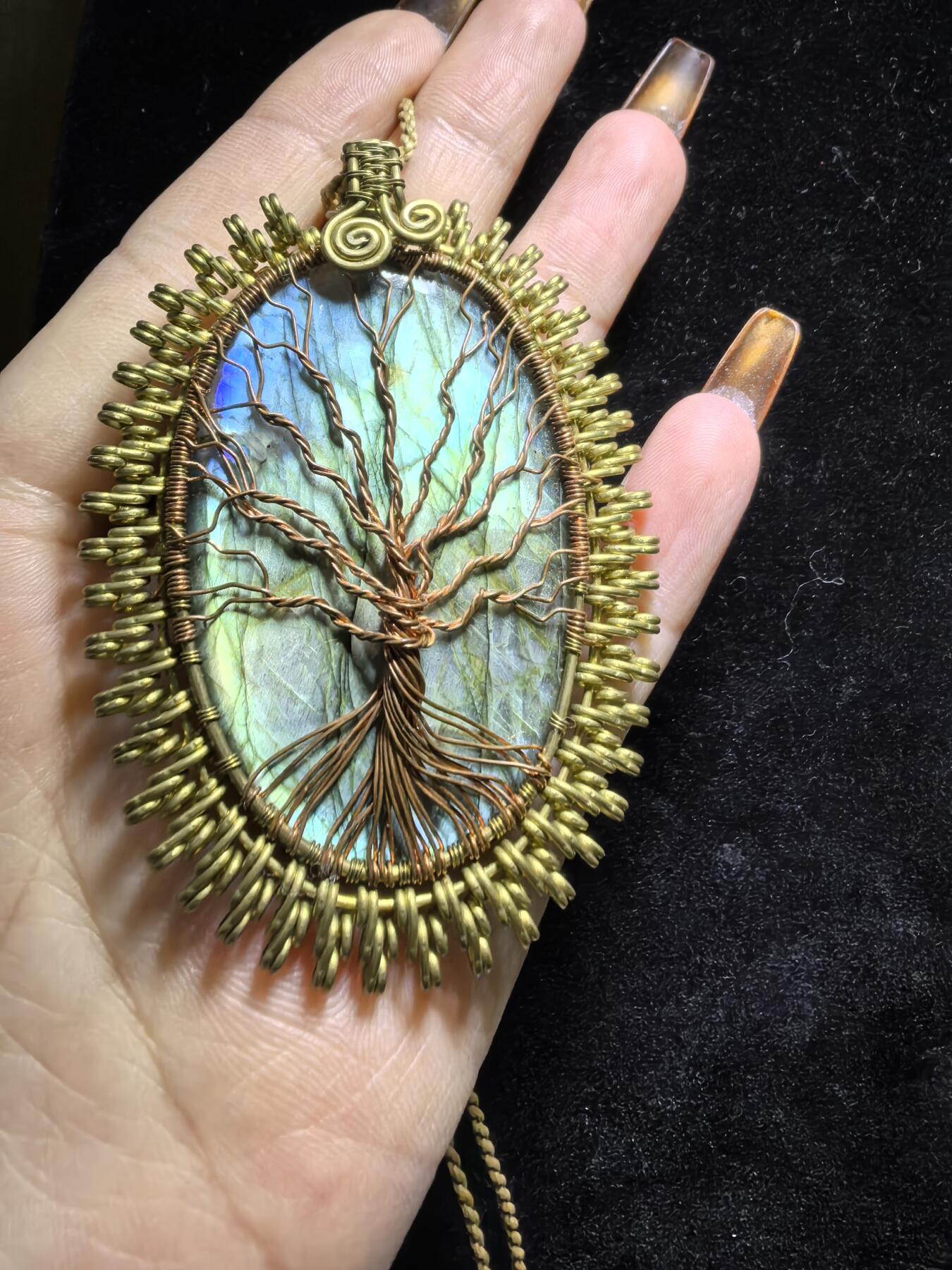 委内瑞拉国际友人纯手工绕丝工艺《灵光生命之树吊坠》男女款
以铜线手工编织的生命之树坐落在蓝火拉布拉多长石之上，整件作品带来更强的净化与守护能量。采用巴西编绳，可自由调节长度。
一件汇聚光、根与灵性的护符。
​尺寸：7.1cm*5.1cm*0.8cm每一款都是独一无二，非量产。
​天然有机宝石内部无法避免结构纹理等，介意勿扰！