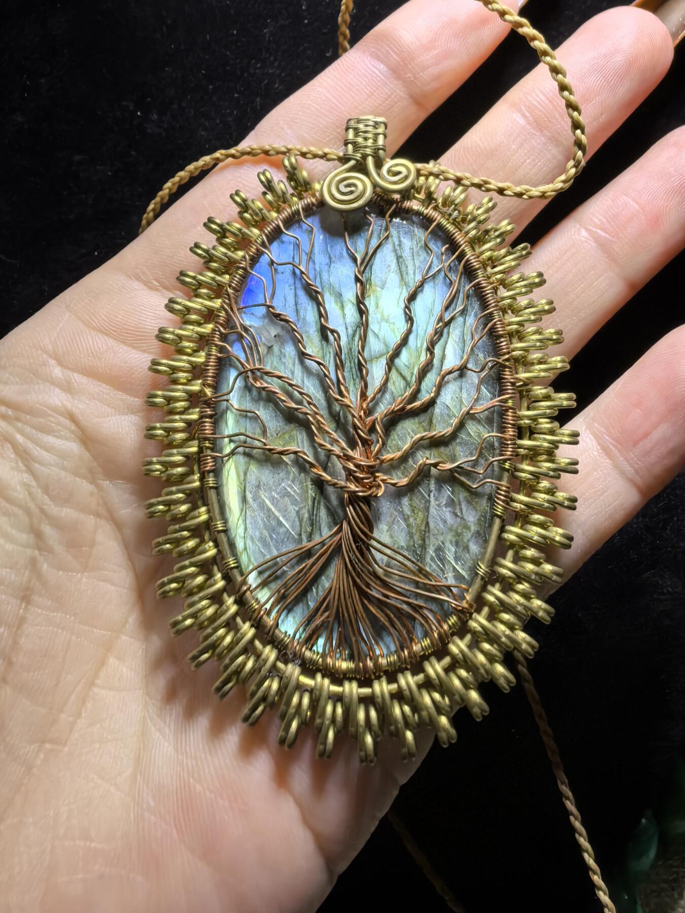 委内瑞拉国际友人纯手工绕丝工艺《灵光生命之树吊坠》男女款
以铜线手工编织的生命之树坐落在蓝火拉布拉多长石之上，整件作品带来更强的净化与守护能量。采用巴西编绳，可自由调节长度。
一件汇聚光、根与灵性的护符。
​尺寸：7.1cm*5.1cm*0.8cm每一款都是独一无二，非量产。
​天然有机宝石内部无法避免结构纹理等，介意勿扰！