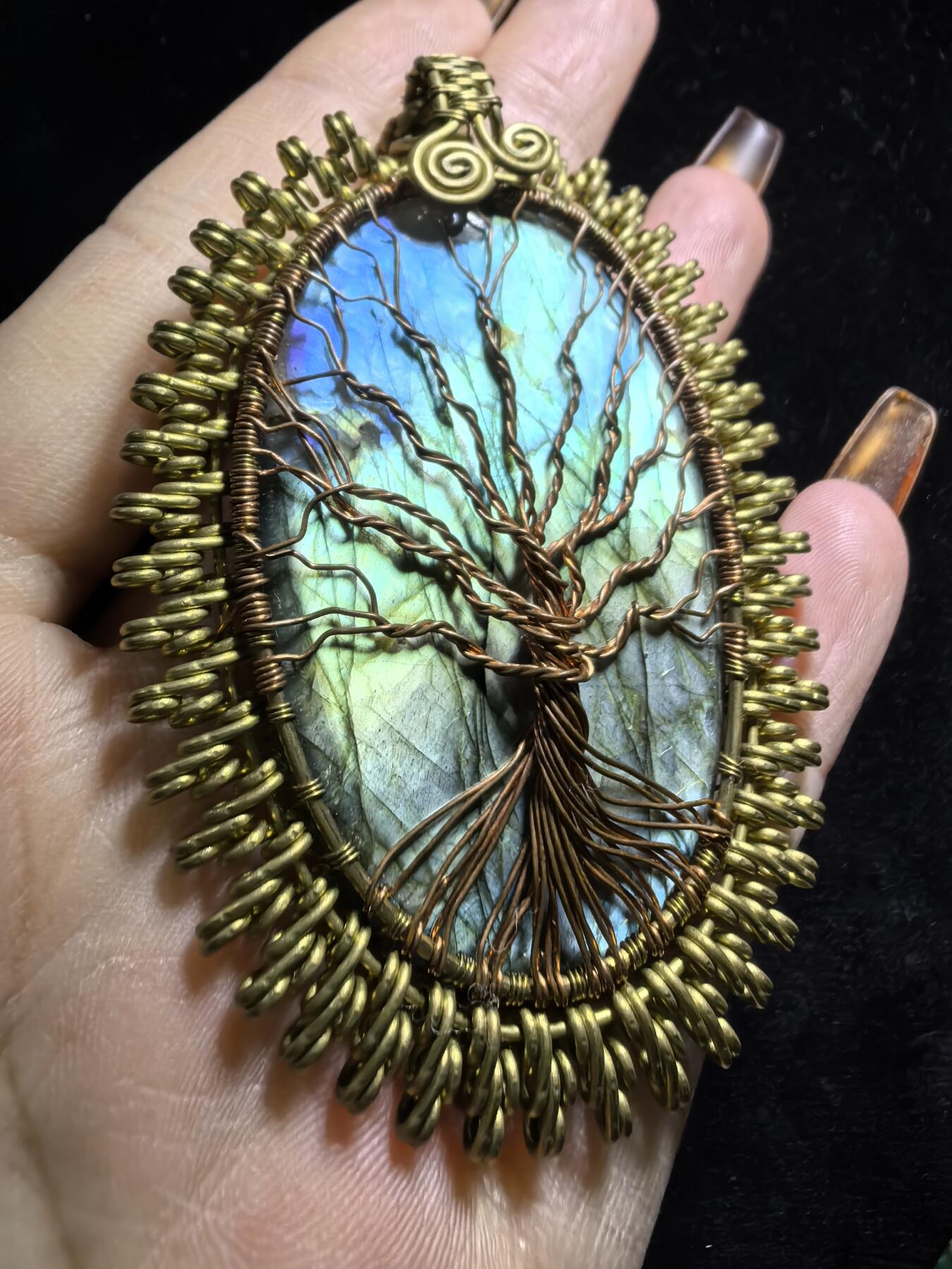 委内瑞拉国际友人纯手工绕丝工艺《灵光生命之树吊坠》男女款
以铜线手工编织的生命之树坐落在蓝火拉布拉多长石之上，整件作品带来更强的净化与守护能量。采用巴西编绳，可自由调节长度。
一件汇聚光、根与灵性的护符。
​尺寸：7.1cm*5.1cm*0.8cm每一款都是独一无二，非量产。
​天然有机宝石内部无法避免结构纹理等，介意勿扰！