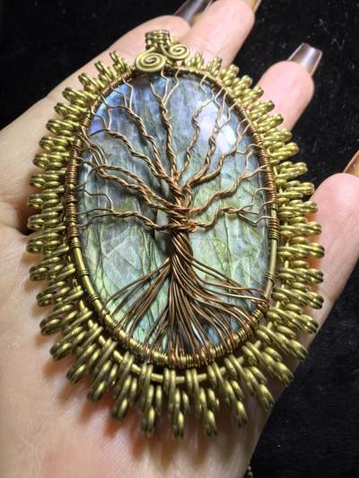 委内瑞拉国际友人纯手工绕丝工艺《灵光生命之树吊坠》男女款
以铜线手工编织的生命之树坐落在蓝火拉布拉多长石之上，整件作品带来更强的净化与守护能量。采用巴西编绳，可自由调节长度。
一件汇聚光、根与灵性的护符。
​尺寸：7.1cm*5.1cm*0.8cm每一款都是独一无二，非量产。
​天然有机宝石内部无法避免结构纹理等，介意勿扰！