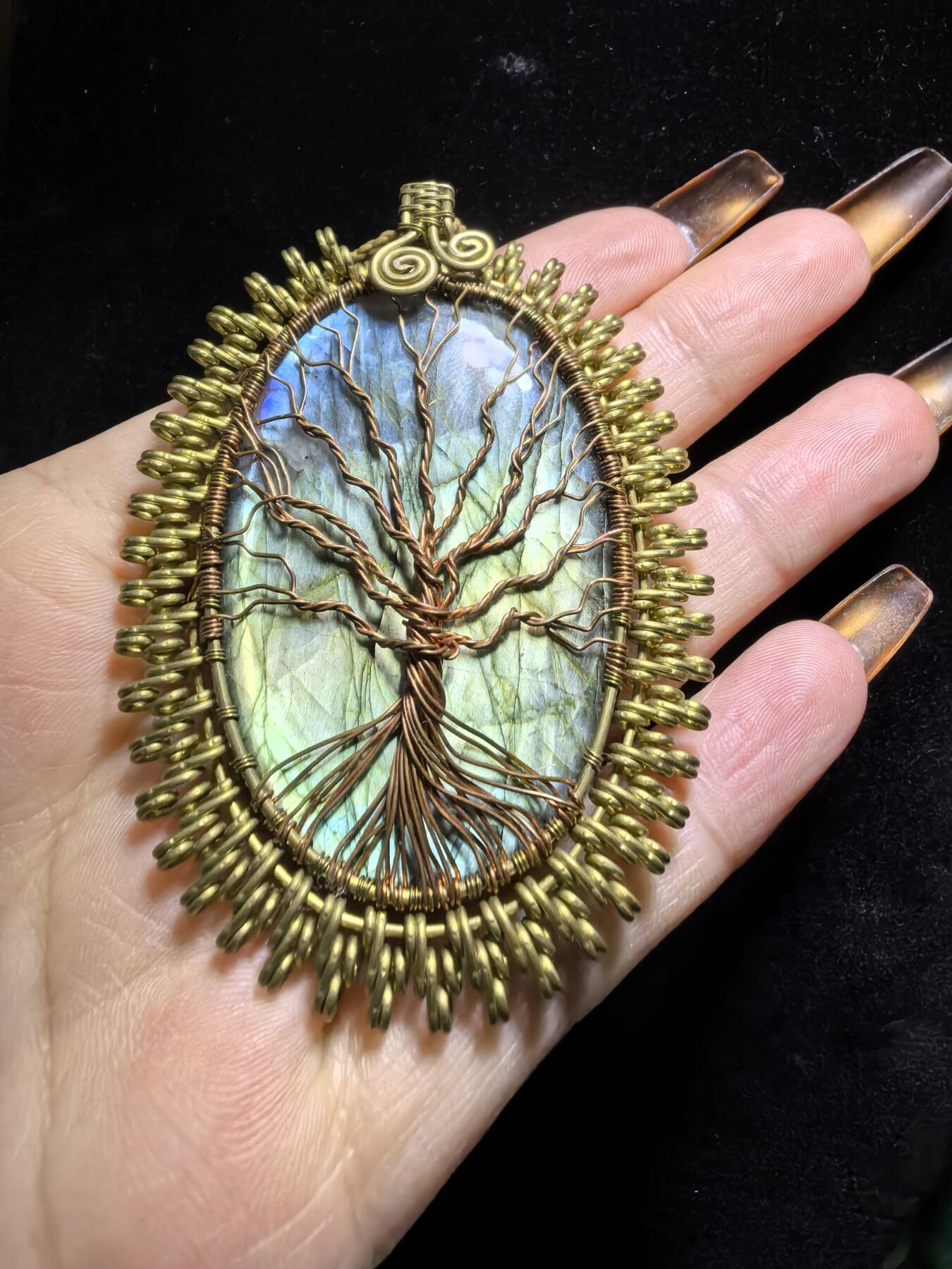 委内瑞拉国际友人纯手工绕丝工艺《灵光生命之树吊坠》男女款
以铜线手工编织的生命之树坐落在蓝火拉布拉多长石之上，整件作品带来更强的净化与守护能量。采用巴西编绳，可自由调节长度。
一件汇聚光、根与灵性的护符。
​尺寸：7.1cm*5.1cm*0.8cm每一款都是独一无二，非量产。
​天然有机宝石内部无法避免结构纹理等，介意勿扰！