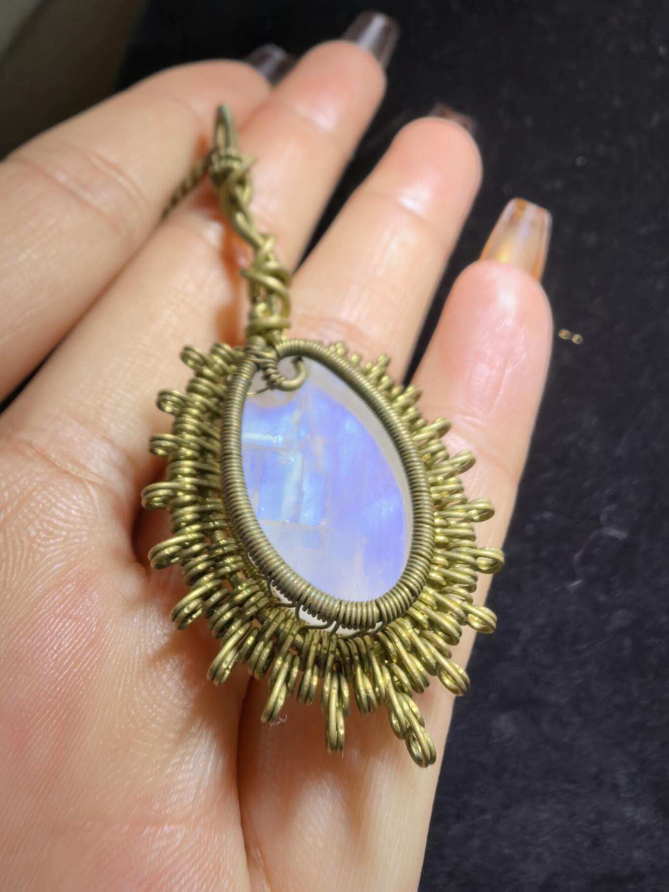 来自委内瑞拉国际友人手工绕丝工艺，月光石吊坠 从不同角度观察，它展现出不同的色彩魅力。有时是极光般的梦幻色彩，有时是少女般的温柔色彩，还有时是落日晚霞般的绚烂色彩。 佩戴与众不同独一无二。 尺寸:2.9cm*2.6cm*1.9cm ​