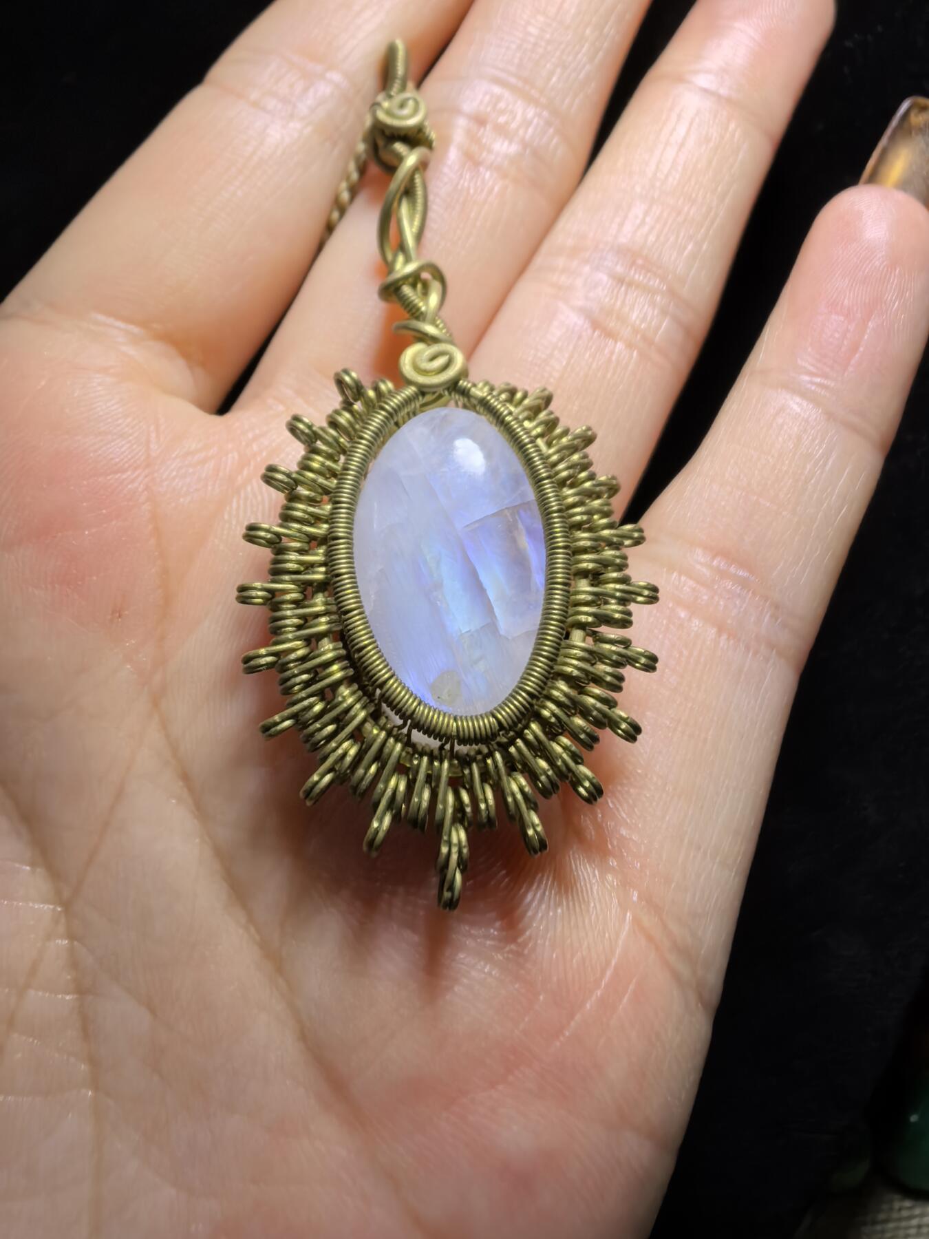 来自委内瑞拉国际友人手工绕丝工艺，月光石吊坠 从不同角度观察，它展现出不同的色彩魅力。有时是极光般的梦幻色彩，有时是少女般的温柔色彩，还有时是落日晚霞般的绚烂色彩。 佩戴与众不同独一无二。 尺寸:2.9cm*2.6cm*1.9cm ​