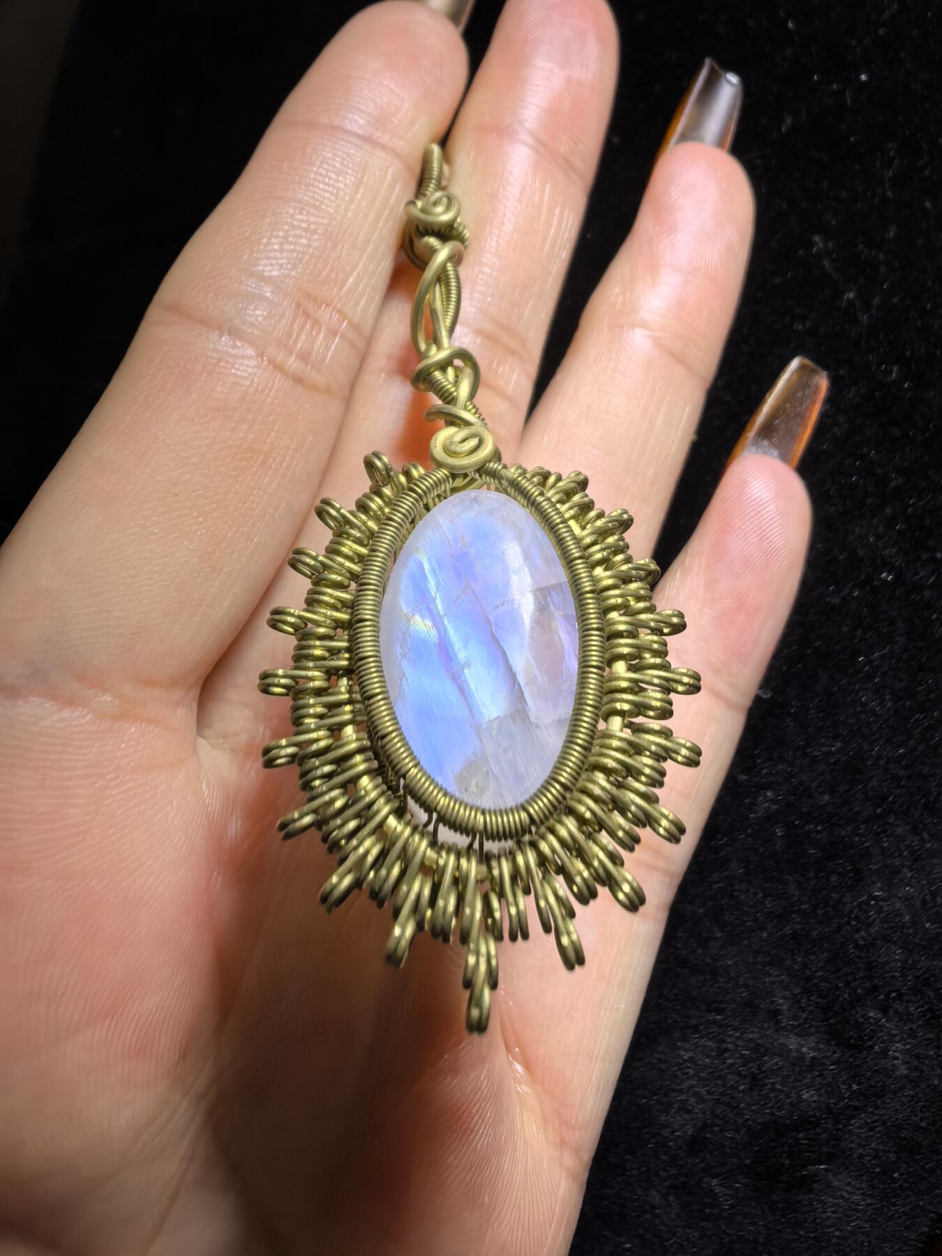 来自委内瑞拉国际友人手工绕丝工艺，月光石吊坠 从不同角度观察，它展现出不同的色彩魅力。有时是极光般的梦幻色彩，有时是少女般的温柔色彩，还有时是落日晚霞般的绚烂色彩。 佩戴与众不同独一无二。 尺寸:2.9cm*2.6cm*1.9cm ​