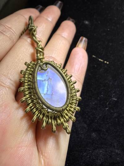 来自委内瑞拉国际友人手工绕丝工艺，月光石吊坠 从不同角度观察，它展现出不同的色彩魅力。有时是极光般的梦幻色彩，有时是少女般的温柔色彩，还有时是落日晚霞般的绚烂色彩。 佩戴与众不同独一无二。 尺寸:2.9cm*2.6cm*1.9cm ​