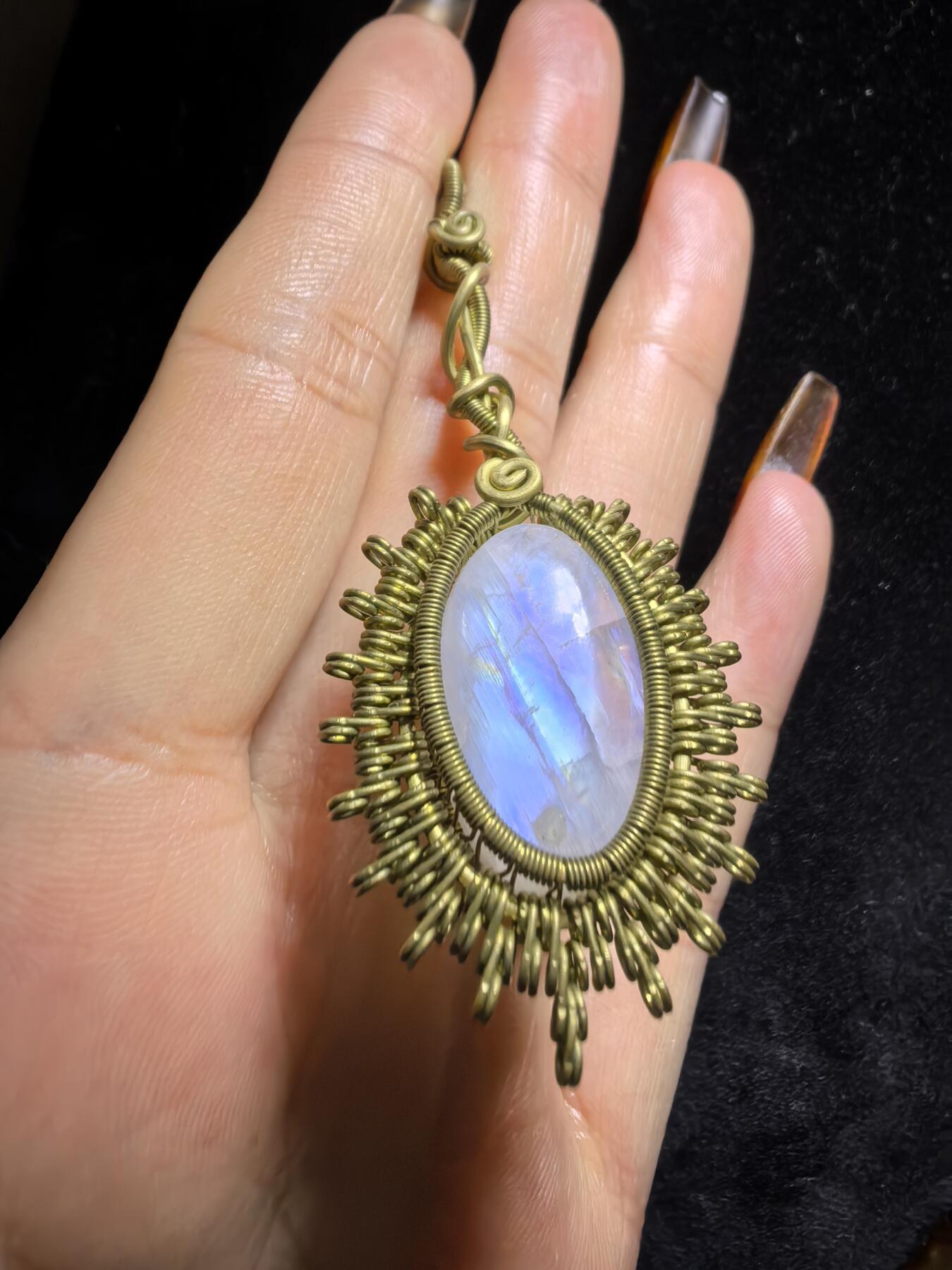 来自委内瑞拉国际友人手工绕丝工艺，月光石吊坠 从不同角度观察，它展现出不同的色彩魅力。有时是极光般的梦幻色彩，有时是少女般的温柔色彩，还有时是落日晚霞般的绚烂色彩。 佩戴与众不同独一无二。 尺寸:2.9cm*2.6cm*1.9cm ​