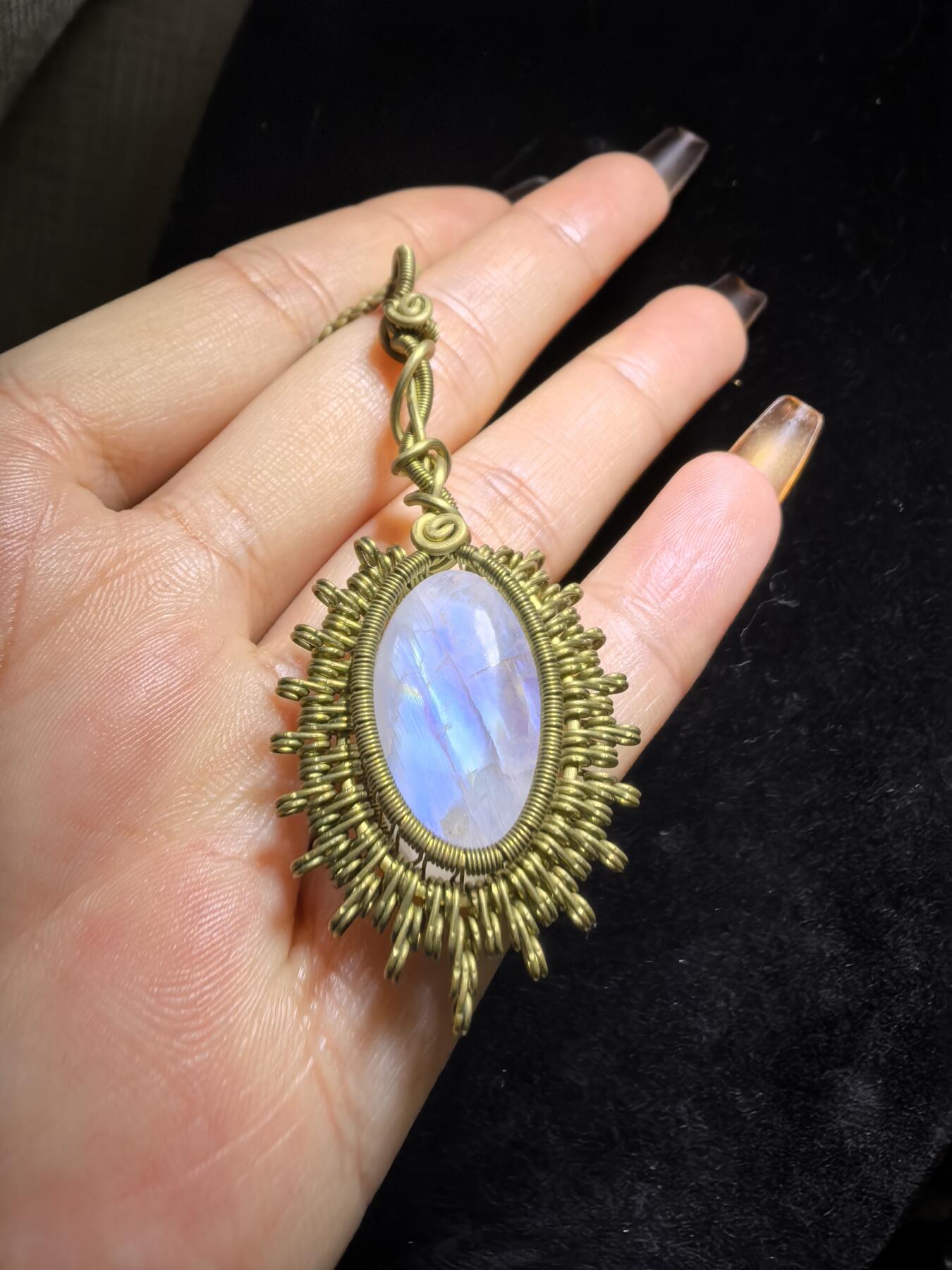 来自委内瑞拉国际友人手工绕丝工艺，月光石吊坠 从不同角度观察，它展现出不同的色彩魅力。有时是极光般的梦幻色彩，有时是少女般的温柔色彩，还有时是落日晚霞般的绚烂色彩。 佩戴与众不同独一无二。 尺寸:2.9cm*2.6cm*1.9cm ​