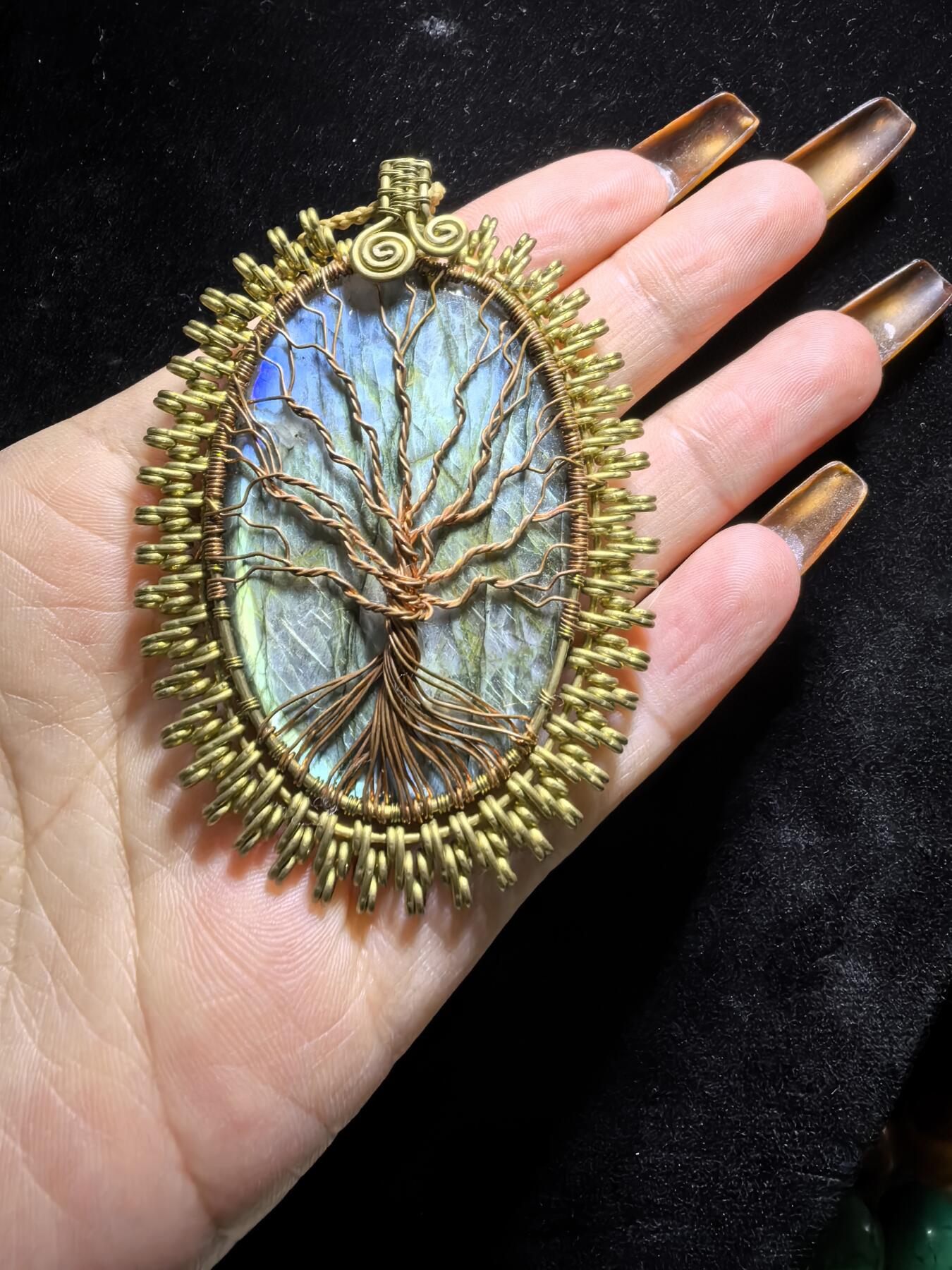 委内瑞拉国际友人纯手工绕丝工艺《灵光生命之树吊坠》男女款
以铜线手工编织的生命之树坐落在蓝火拉布拉多长石之上，整件作品带来更强的净化与守护能量。采用巴西编绳，可自由调节长度。
一件汇聚光、根与灵性的护符。
​尺寸：7.1cm*5.1cm*0.8cm每一款都是独一无二，非量产。
​天然有机宝石内部无法避免结构纹理等，介意勿扰！