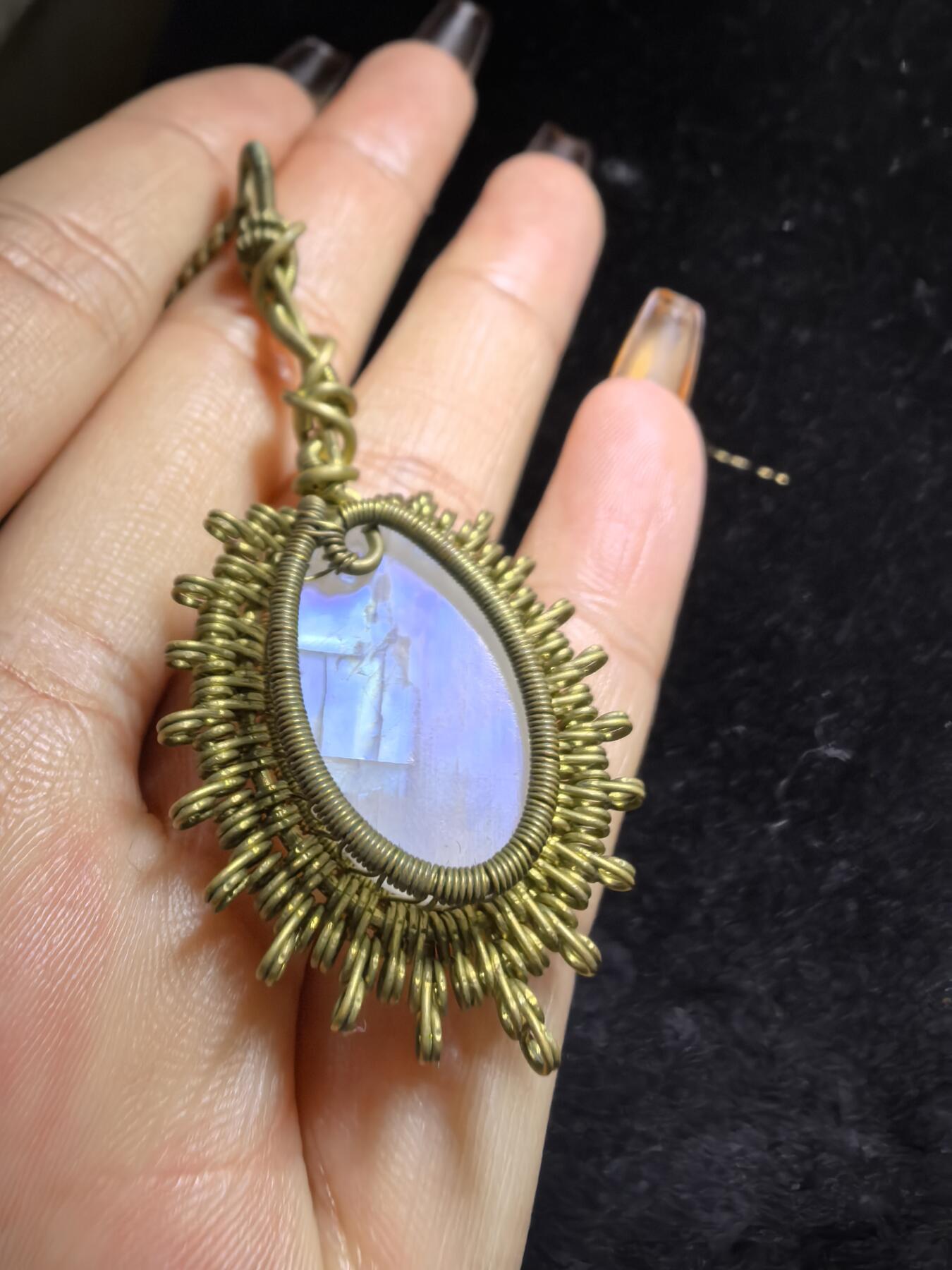 来自委内瑞拉国际友人手工绕丝工艺，月光石吊坠 从不同角度观察，它展现出不同的色彩魅力。有时是极光般的梦幻色彩，有时是少女般的温柔色彩，还有时是落日晚霞般的绚烂色彩。 佩戴与众不同独一无二。 尺寸:2.9cm*2.6cm*1.9cm ​