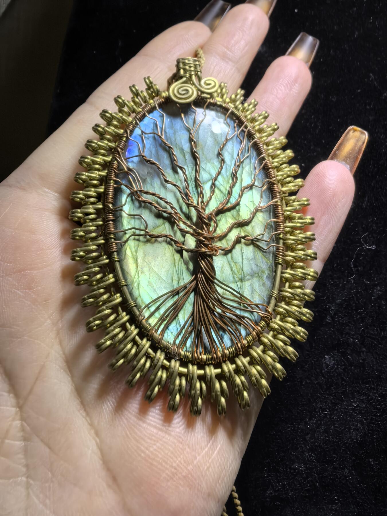 委内瑞拉国际友人纯手工绕丝工艺《灵光生命之树吊坠》男女款
以铜线手工编织的生命之树坐落在蓝火拉布拉多长石之上，整件作品带来更强的净化与守护能量。采用巴西编绳，可自由调节长度。
一件汇聚光、根与灵性的护符。
​尺寸：7.1cm*5.1cm*0.8cm每一款都是独一无二，非量产。
​天然有机宝石内部无法避免结构纹理等，介意勿扰！