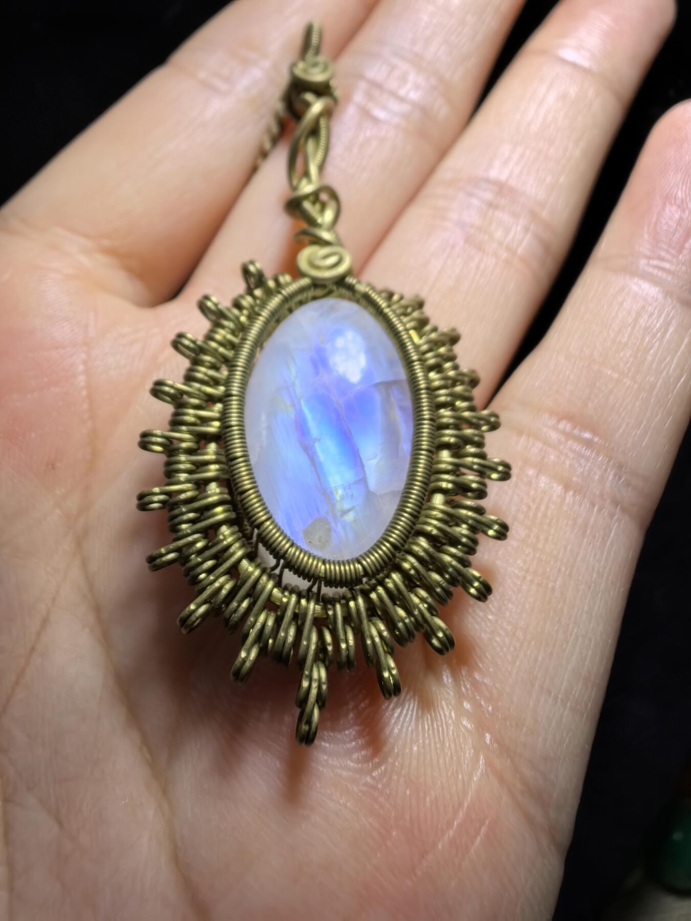 来自委内瑞拉国际友人手工绕丝工艺，月光石吊坠 从不同角度观察，它展现出不同的色彩魅力。有时是极光般的梦幻色彩，有时是少女般的温柔色彩，还有时是落日晚霞般的绚烂色彩。 佩戴与众不同独一无二。 尺寸:2.9cm*2.6cm*1.9cm ​