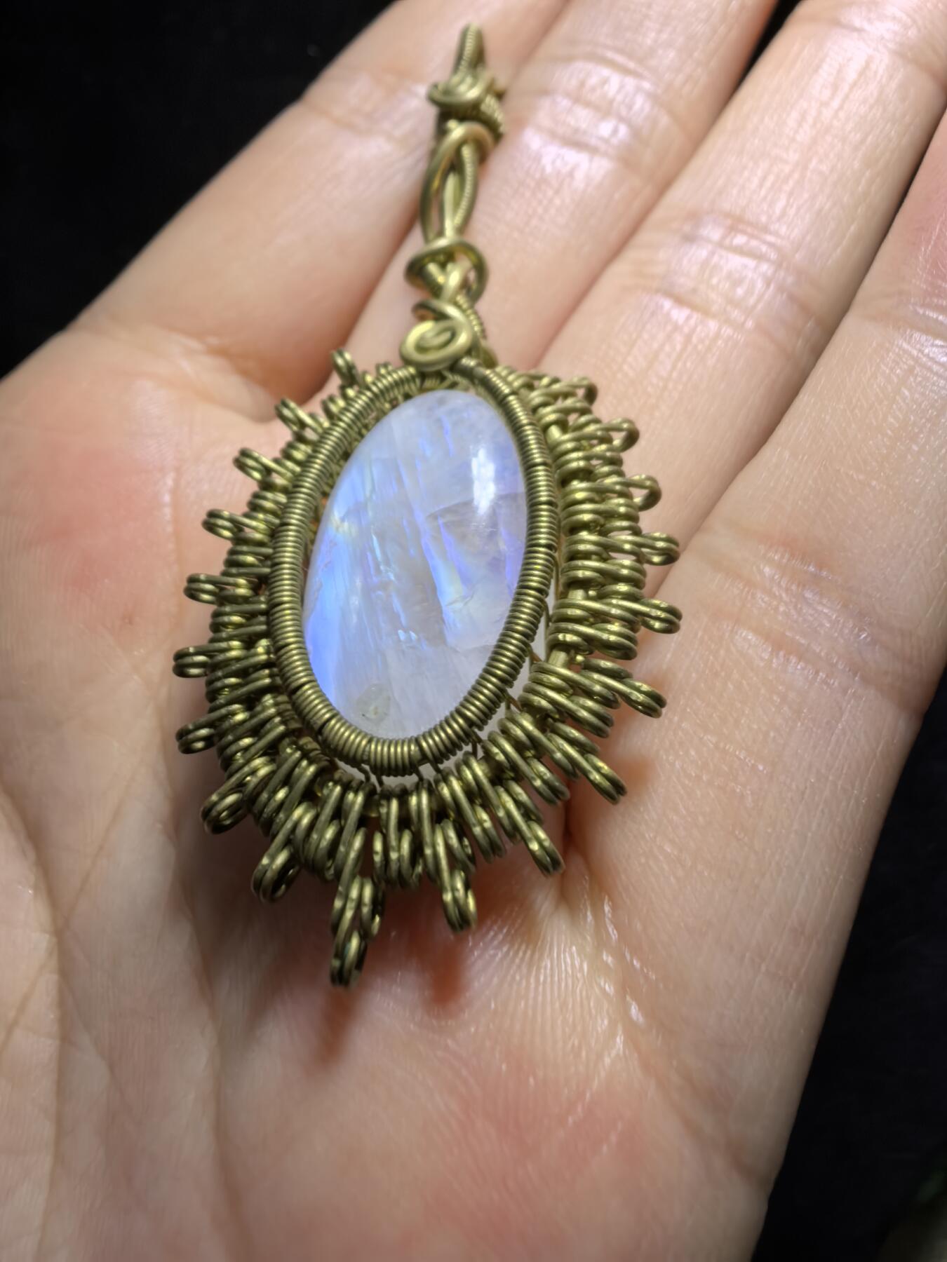 来自委内瑞拉国际友人手工绕丝工艺，月光石吊坠 从不同角度观察，它展现出不同的色彩魅力。有时是极光般的梦幻色彩，有时是少女般的温柔色彩，还有时是落日晚霞般的绚烂色彩。 佩戴与众不同独一无二。 尺寸:2.9cm*2.6cm*1.9cm ​